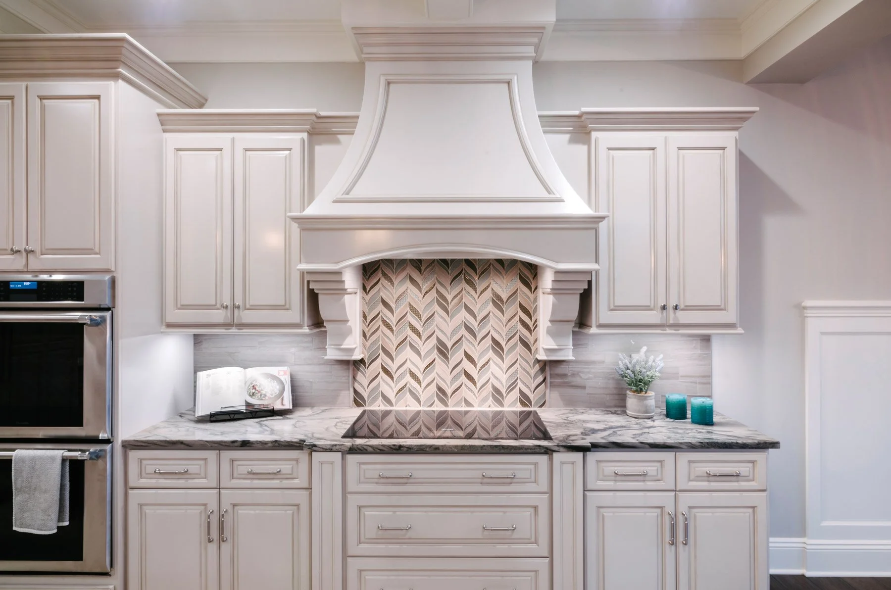 Induction range on quartz countertops with custom cabinets, decorative vent hood cover, and wall ovens