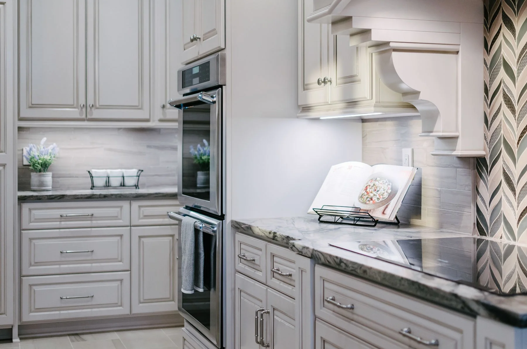 Custom kitchen wall with induction countertop range, wall ovens, and off-white cabinetry