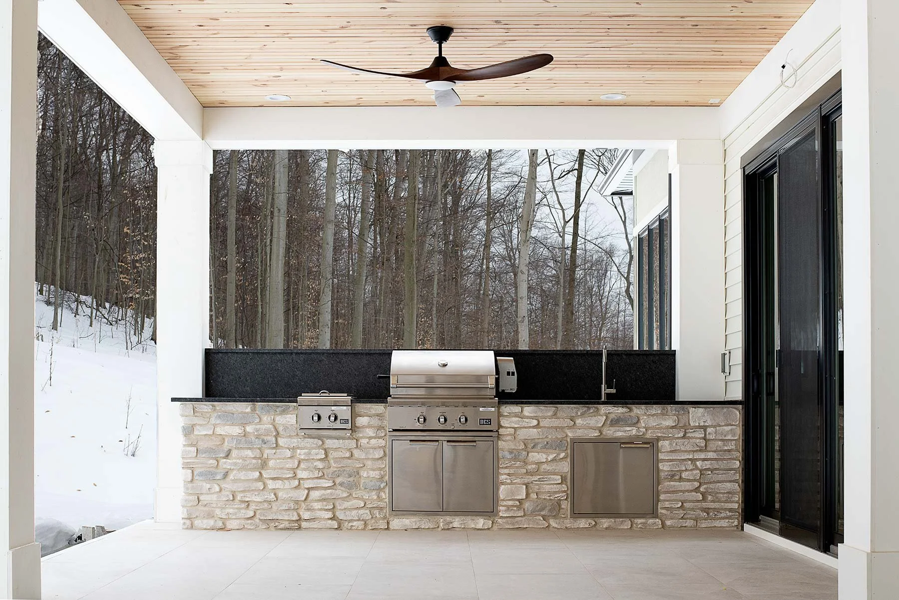 Spacious covered outdoor kitchen with stone cabinetry, stainless appliances, and forest views, providing design inspiration and outdoor spaces for year-round use.