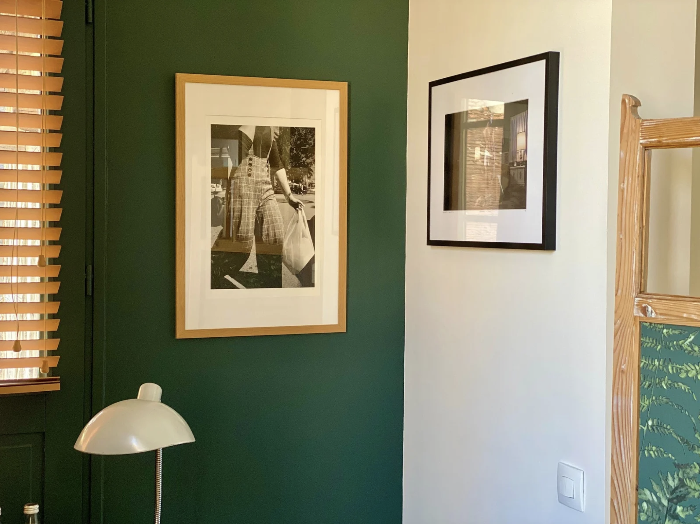 Une décoration intérieure avec une peinture noir et blanc représentant une personne portant un pantalon à carreaux, un cadre noir avec une photo réfléchissante, un lampadaire blanc et des volets en bois dans une pièce.