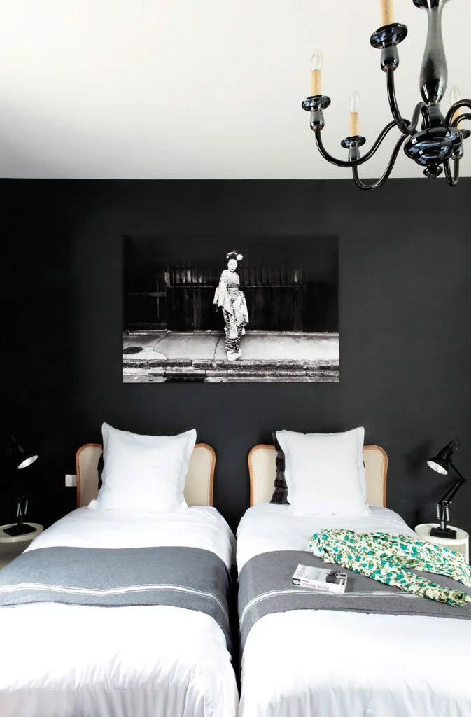 Chambre avec deux lits jumeaux, une peinture en noir et blanc d'une femme en kimono au mur, deux lampes de chevet et un chandelier au plafond.