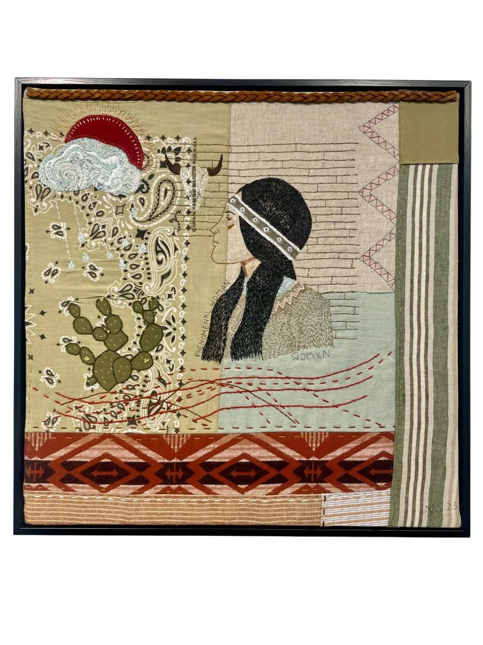 A textile artwork depicting a profile of a woman with long black hair, a headband, and traditional clothing. The background features various patterns, a cactus, a cloud, a red sun or moon, a bull skull, and abstract designs.