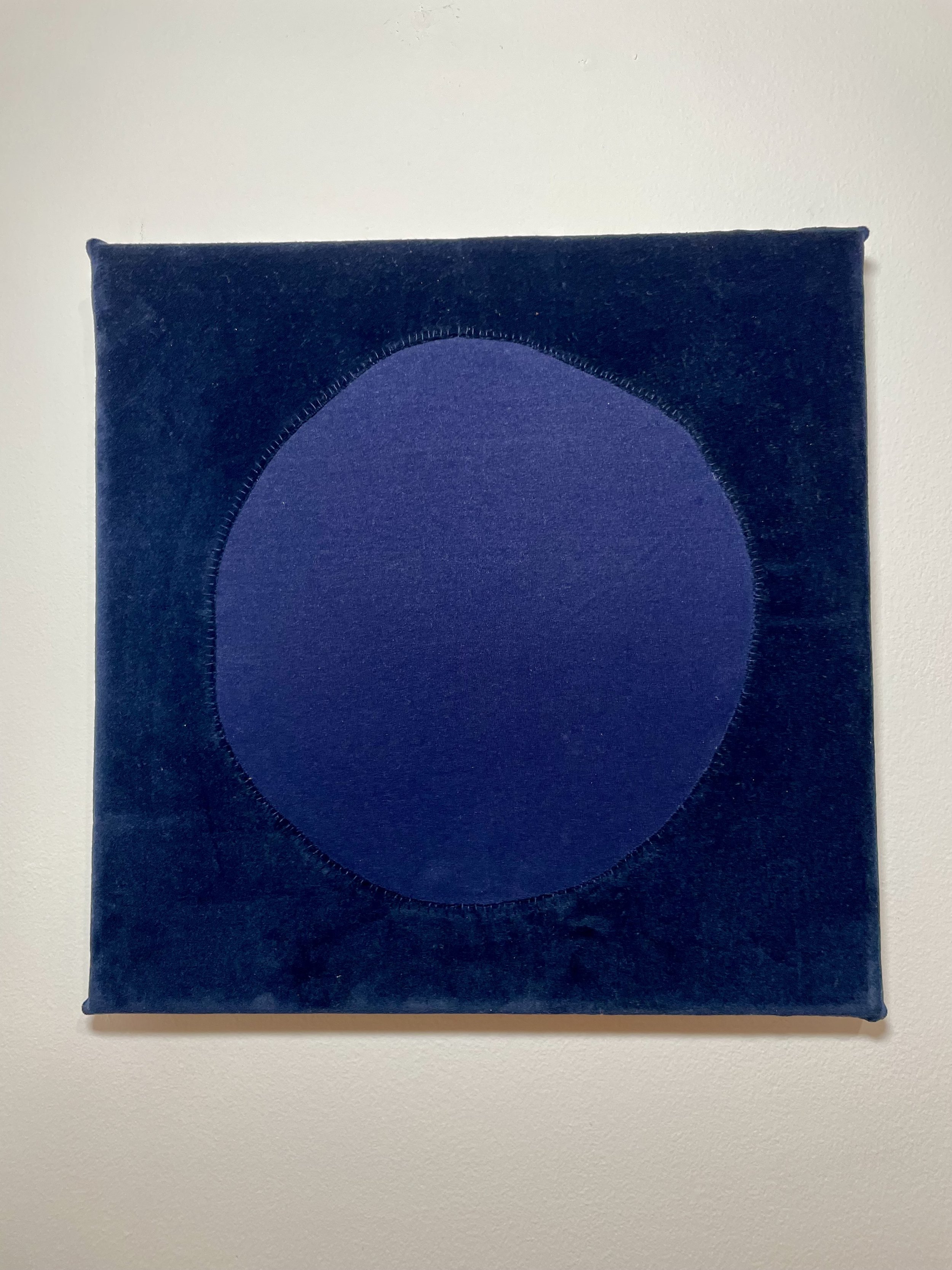 A dark blue square piece of velvet fabric with a large blue circle in the center, mounted on a wall.