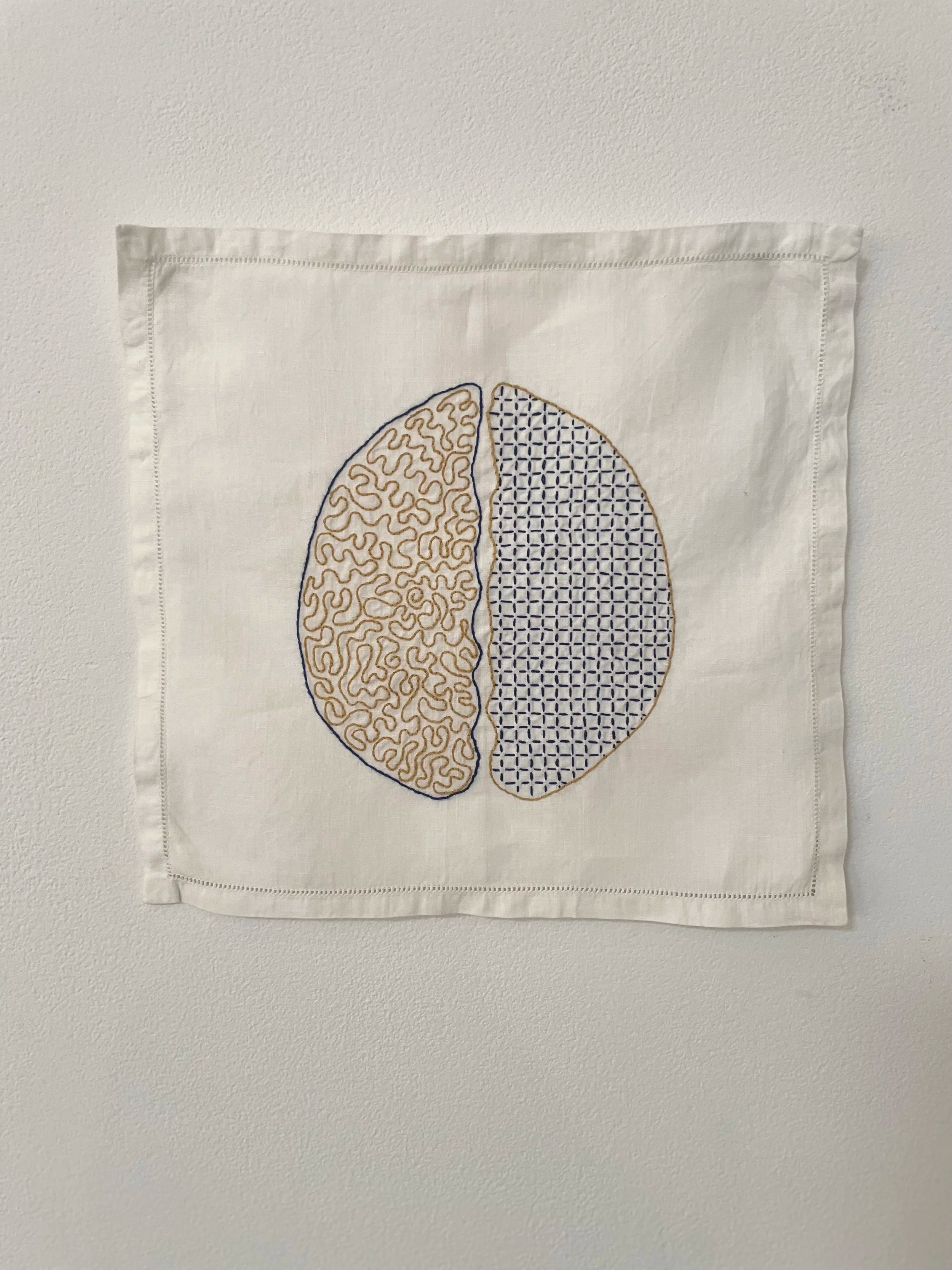 Embroidery in yellow and blue of a split brain on a white vintage dinner napkin.