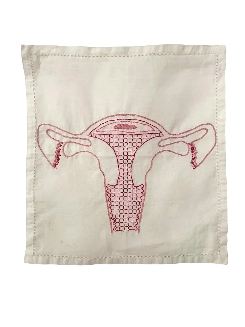 Embroidery of a uterus on a white vintage dinner napkin.