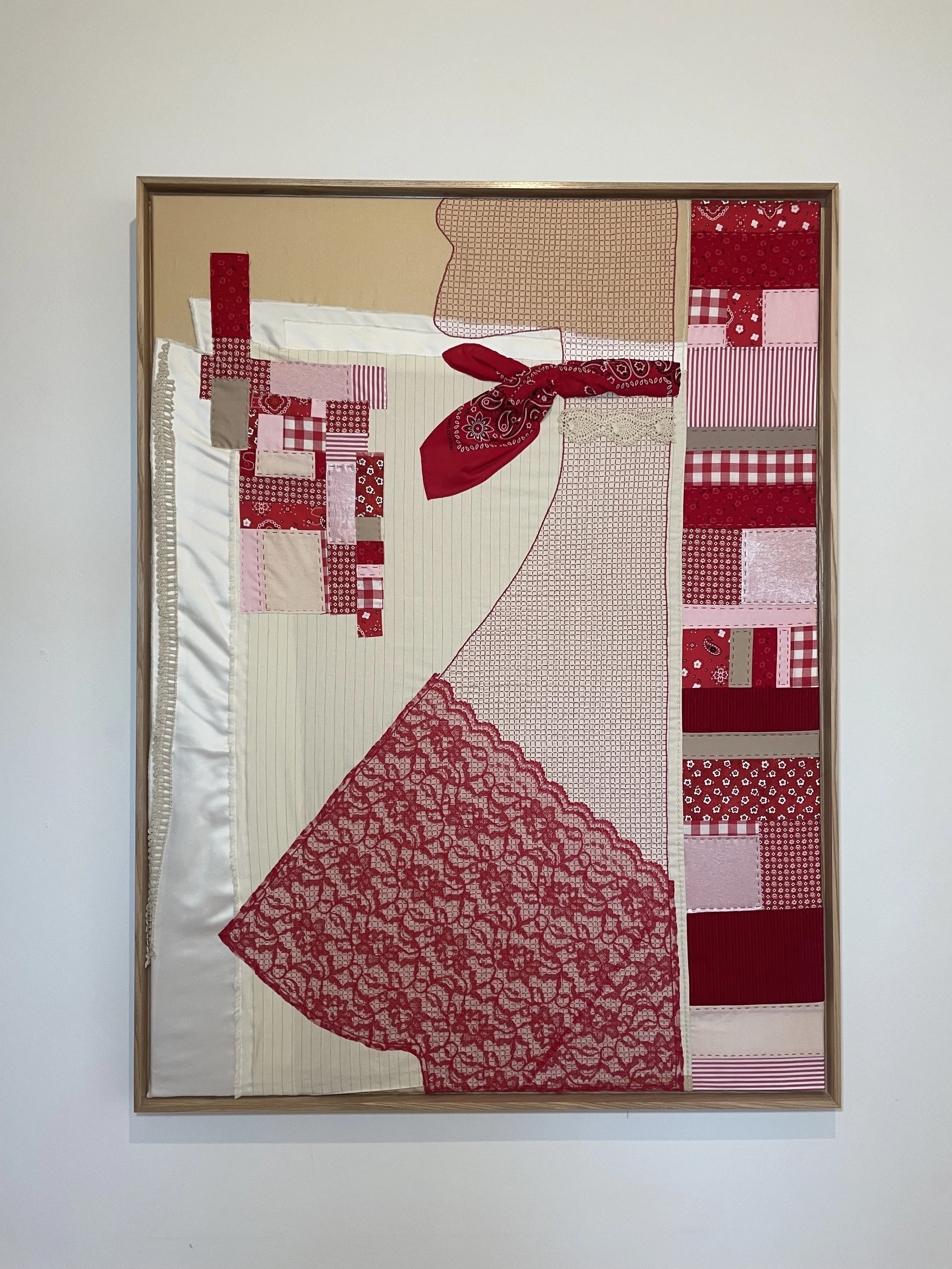 Mixed media textile artwork with a woman shape in red, pink, and beige fabric patches, lace, and a red bandana tied in a bow, framed in wood.