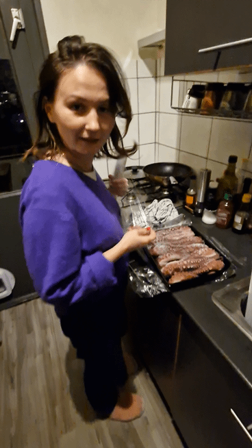 Woman preparing meat in a kitchen with various condiments nearby.