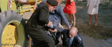 Group of people pulling a man out of muddy water next to a tractor.