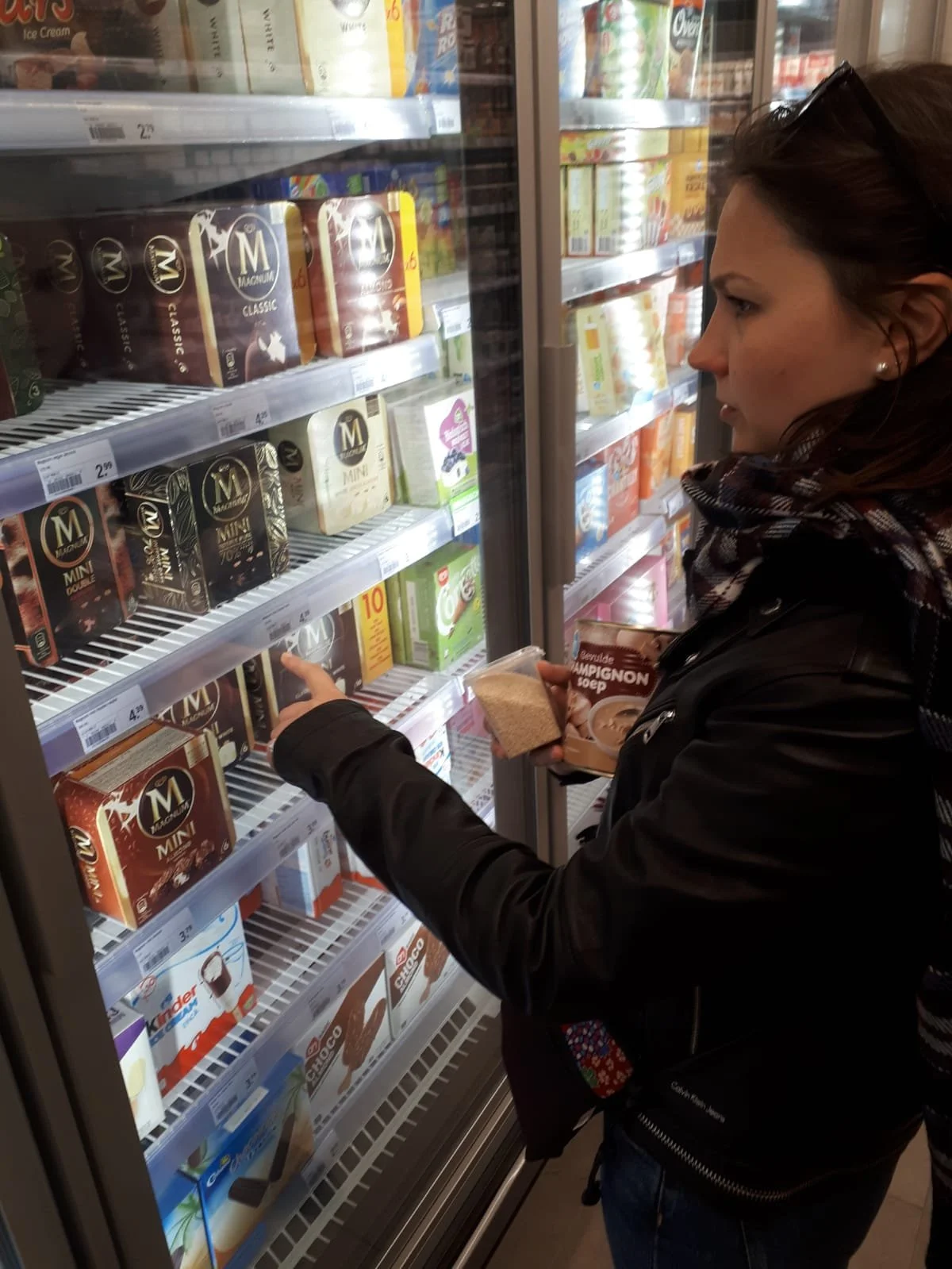 Woman selecting ice cream from a freezer in a store.