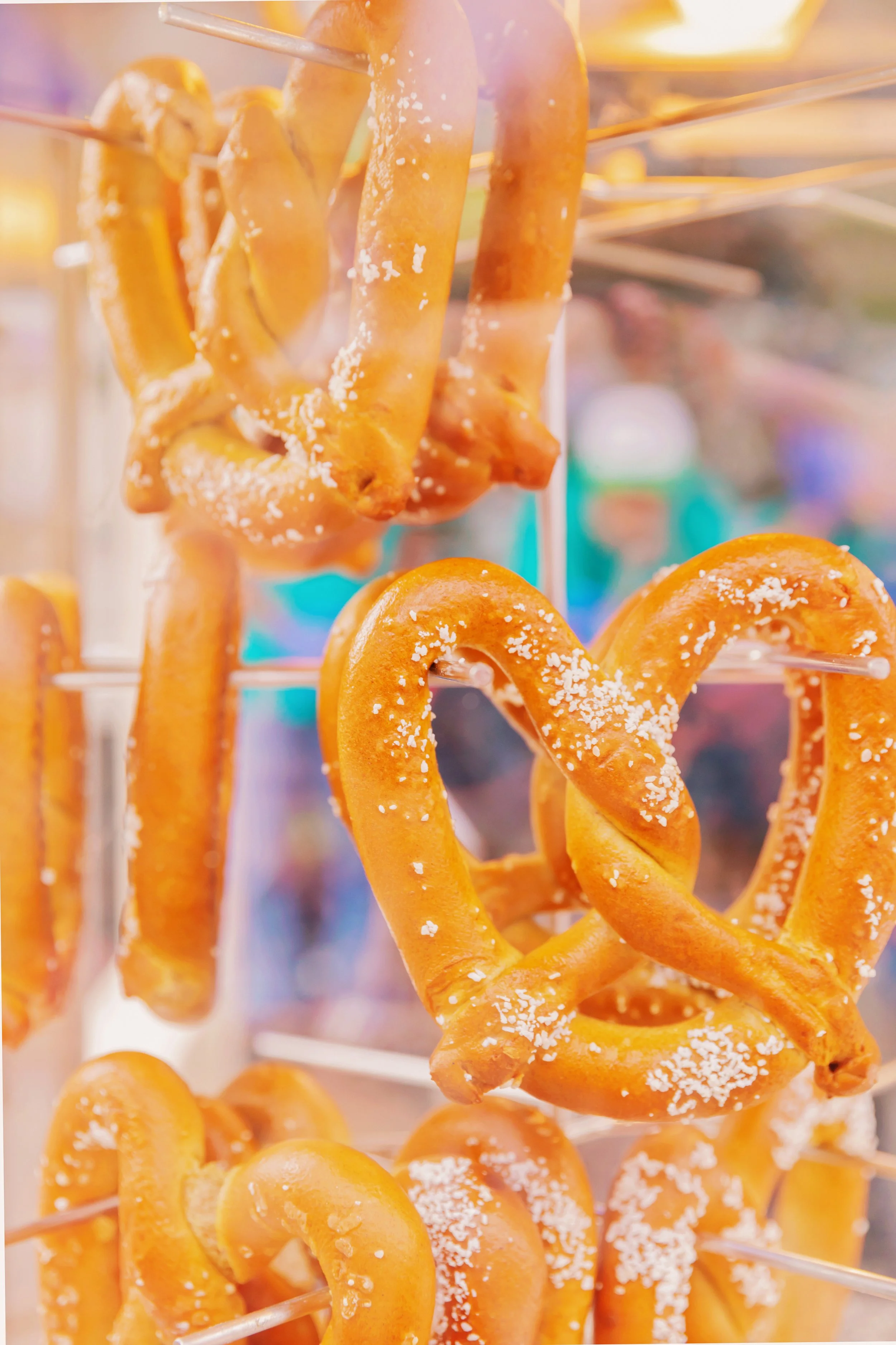 Close-up of salted, caramel-colored pretzels hanging on a display rack at a carnival or fair.