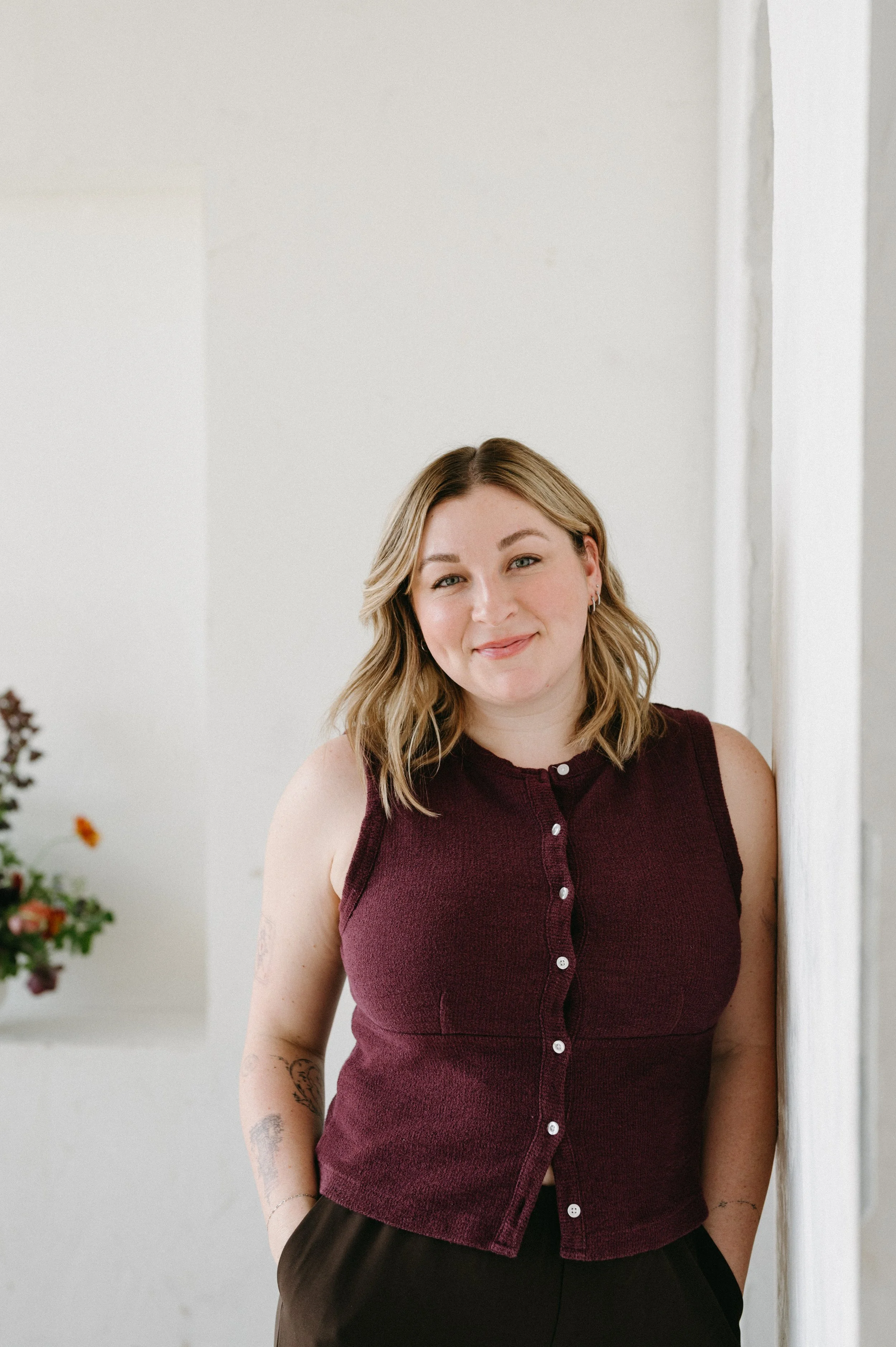 Dr. Shelby Kittinger, a licensed psychologist in Newport Beach, California, standing next to a white wall in a room with minimal decor and flowers visible in the background.