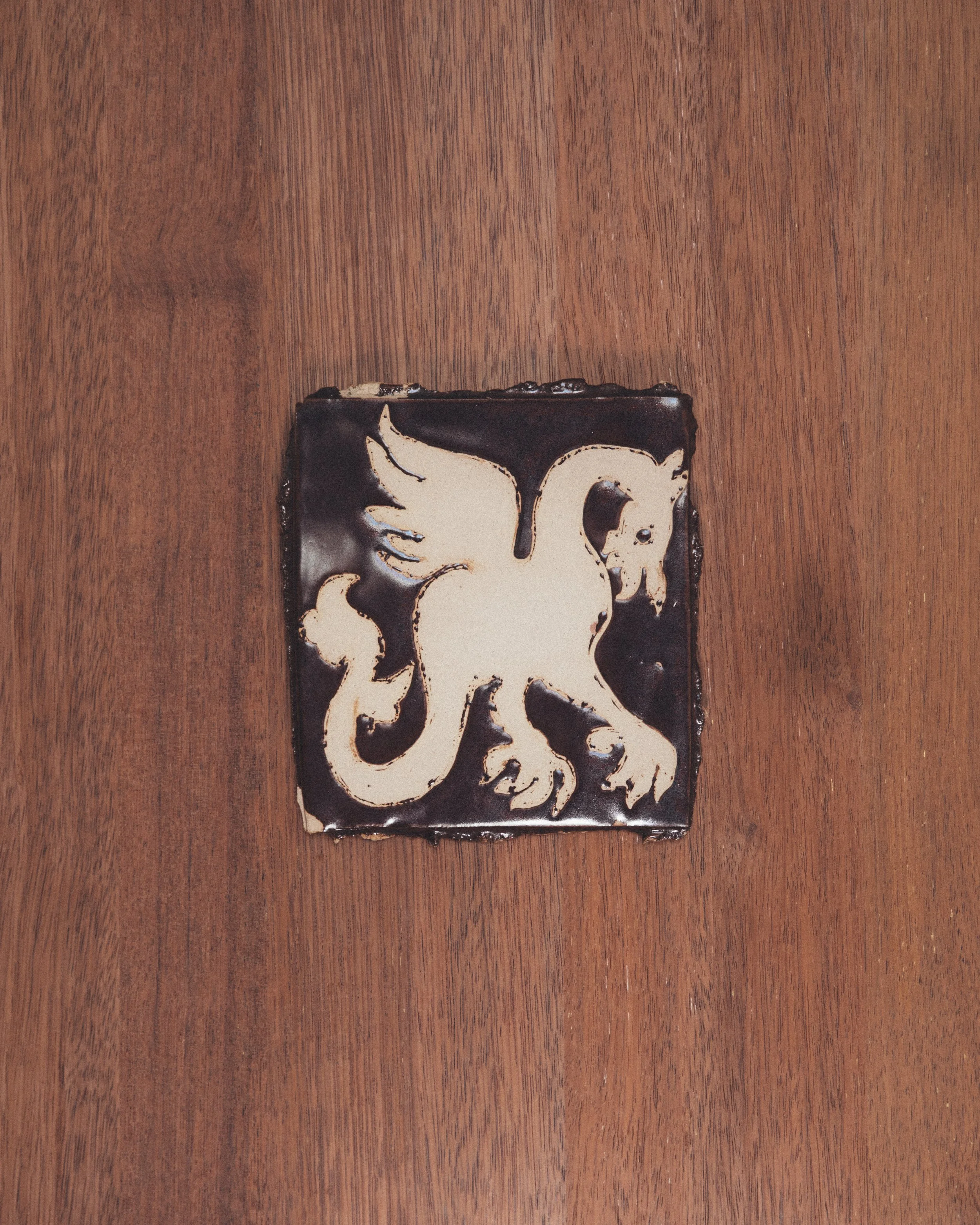 Close-up of a patterned ceramic tile with black and cream swirls on a wooden surface.