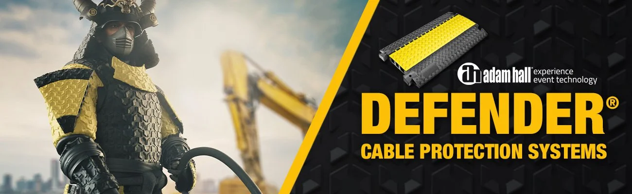 A person wearing protective armor in black and yellow, with a construction excavator in the background, and an advertisement for Adam Hall Defender cable protection systems.