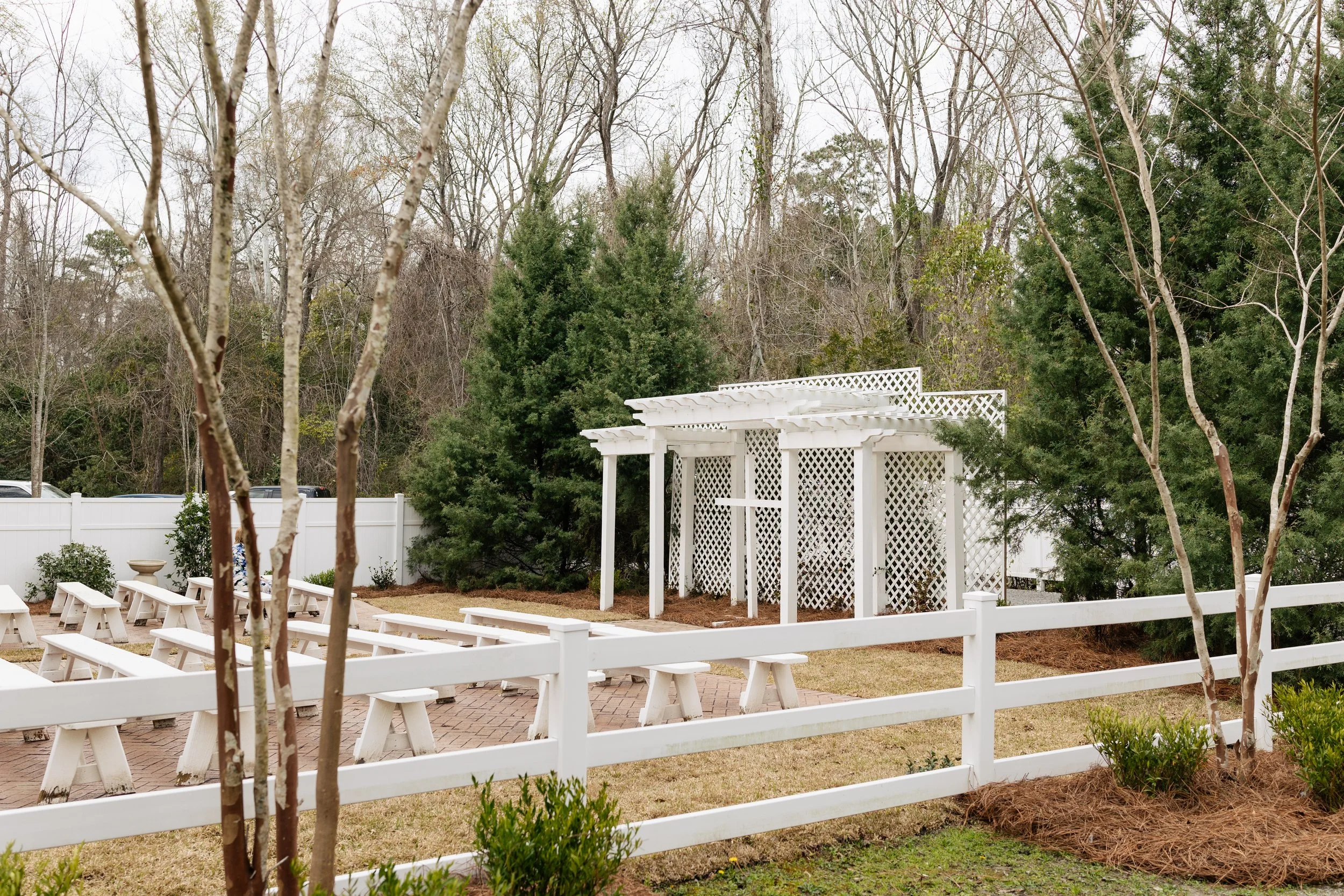 Outdoor wedding ceremony garden at 108 W Main in Moncks Corner, SC with white pergola, benches, and greenery.