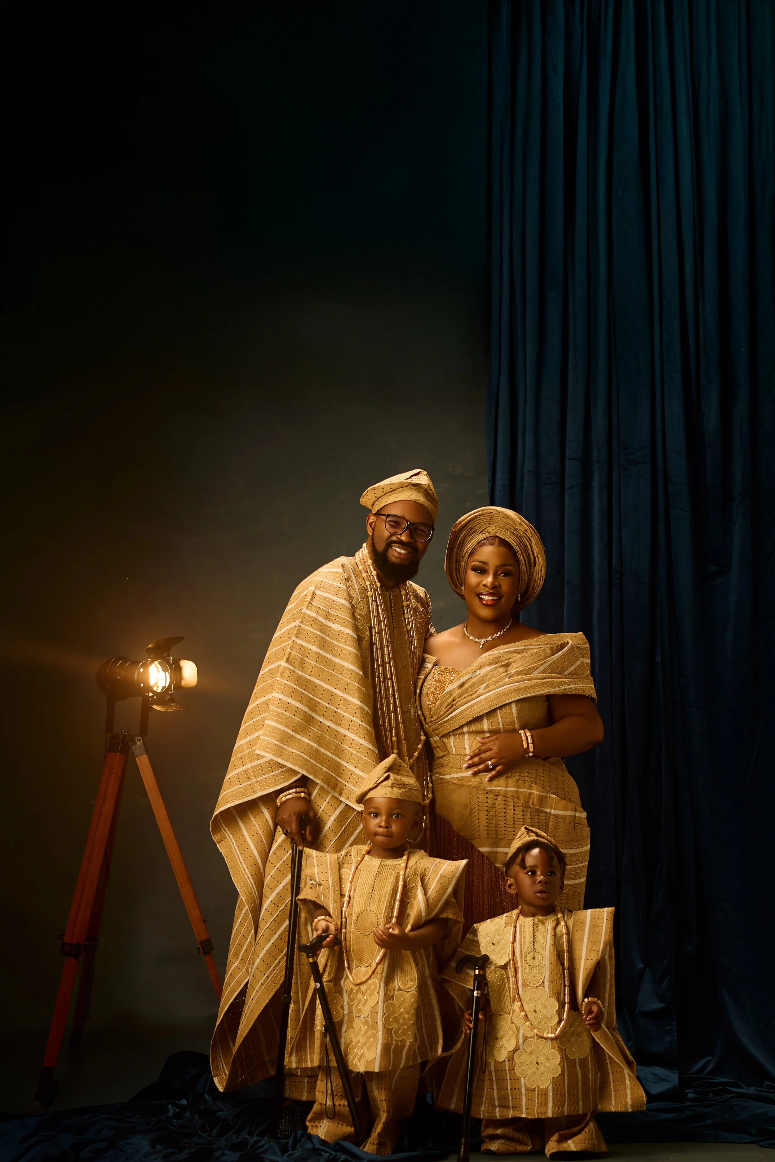 Pregnant woman in a brown dress with a floral headband and tulle robe, posing against a dark, textured background.