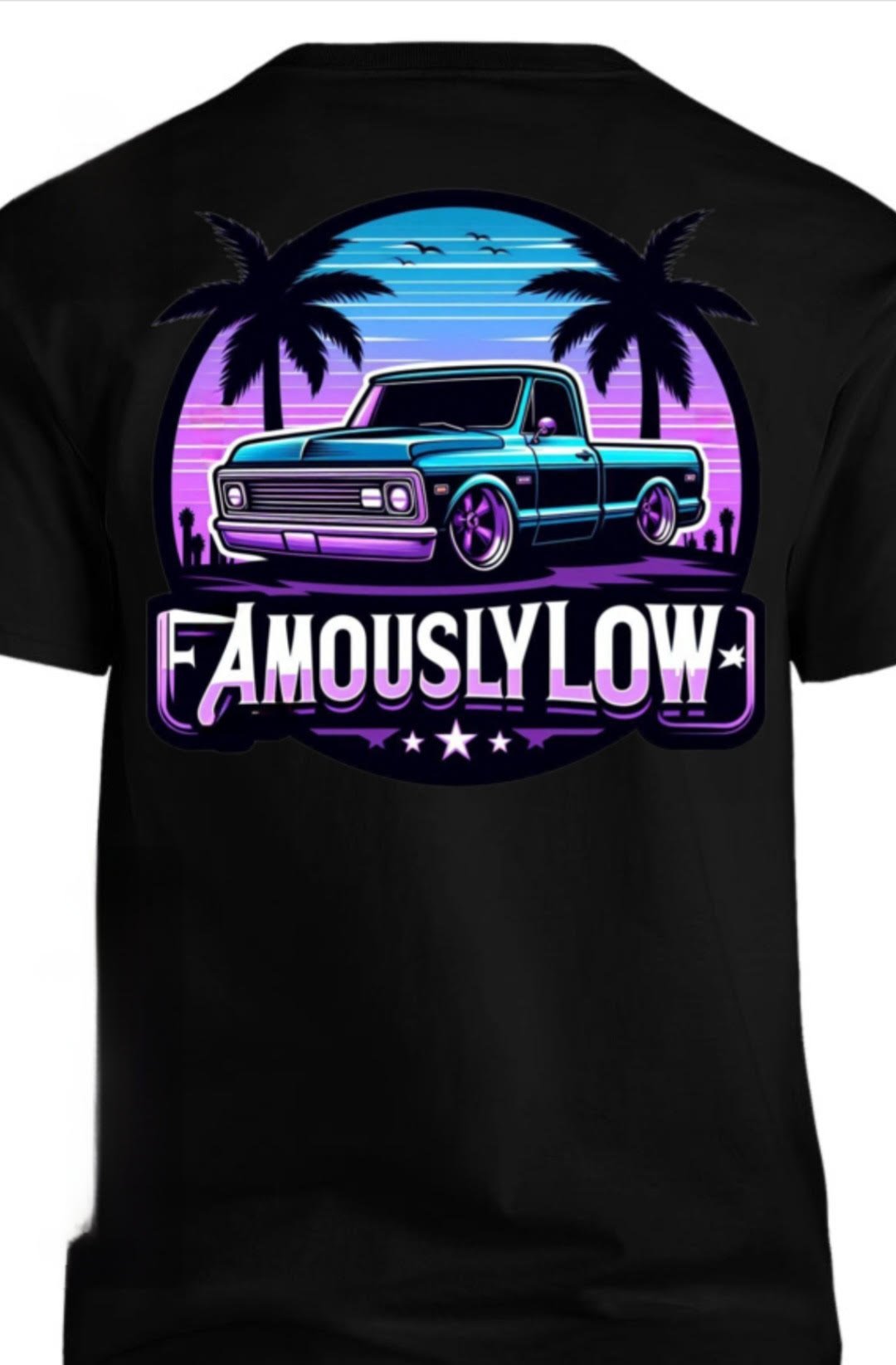 A black T-shirt featuring a digital graphic of a classic pickup truck set against a neon-lit retro sunset background with palm trees, and the phrase 'FAMOUSLY LOW' in bold white and purple lettering.