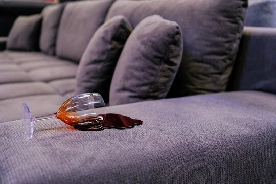 Close up of a glass of red wine spilt on a purple couch