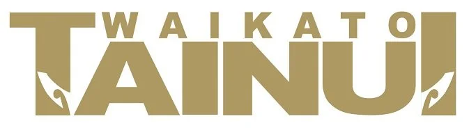 Text saying 'WAIKATO TAINUI' in stylized gold-colored letters with decorative elements on the ends.