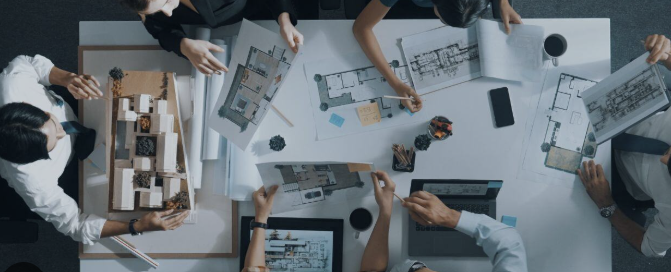 Un groupe de personnes travaillant sur un projet architectural avec des plans, maquettes, ordinateurs et fournitures de bureau sur une table