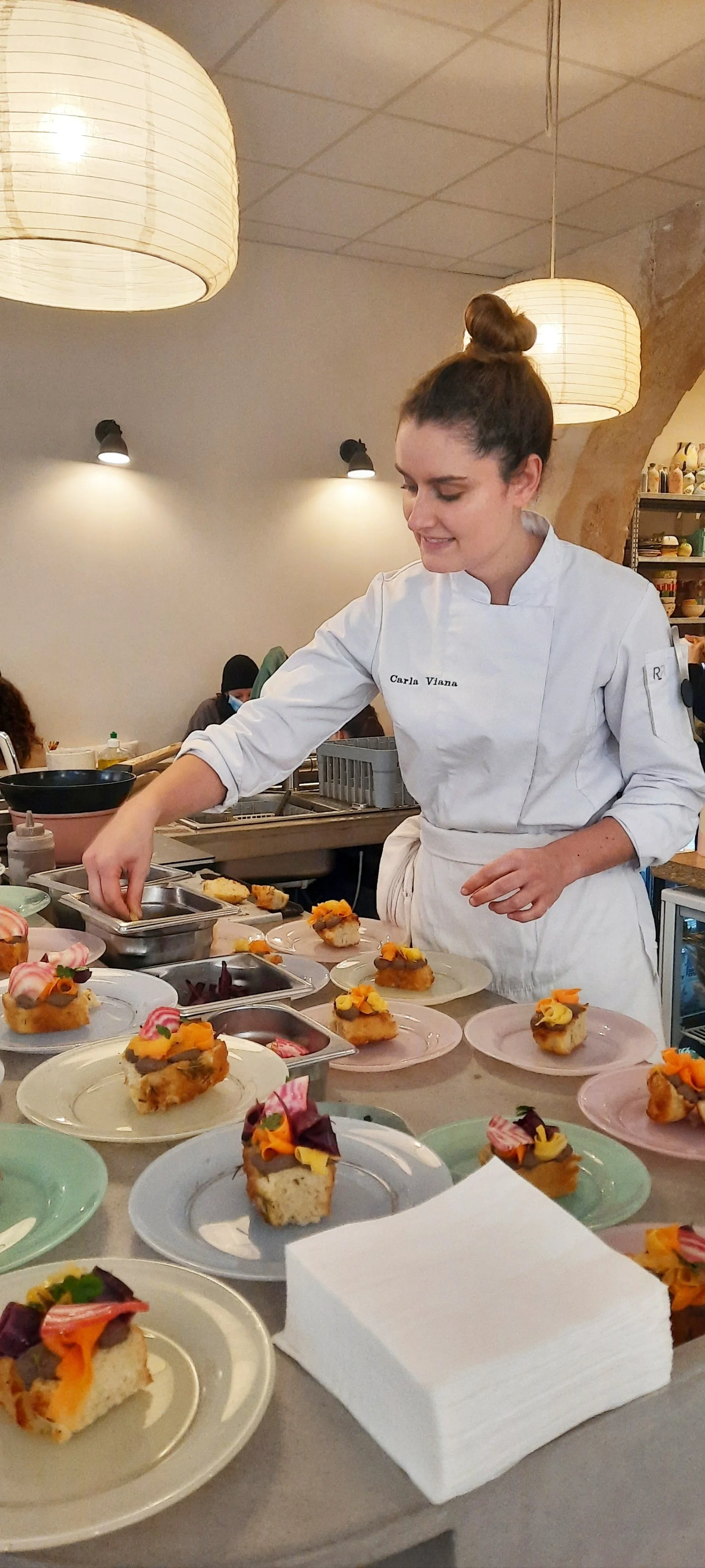 Une chef cuisinière prépare des parts de gâteau décorés sur une table dans une cuisine.