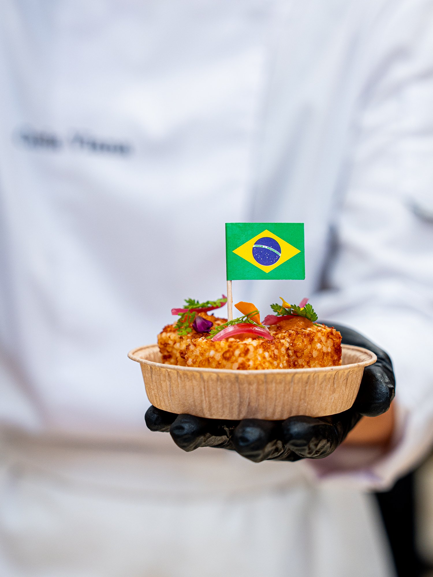 Gourmet plat brésilien avec un drapeau du Brésil, présenté dans un bol en bois, tenu par une personne portant un gant noir.