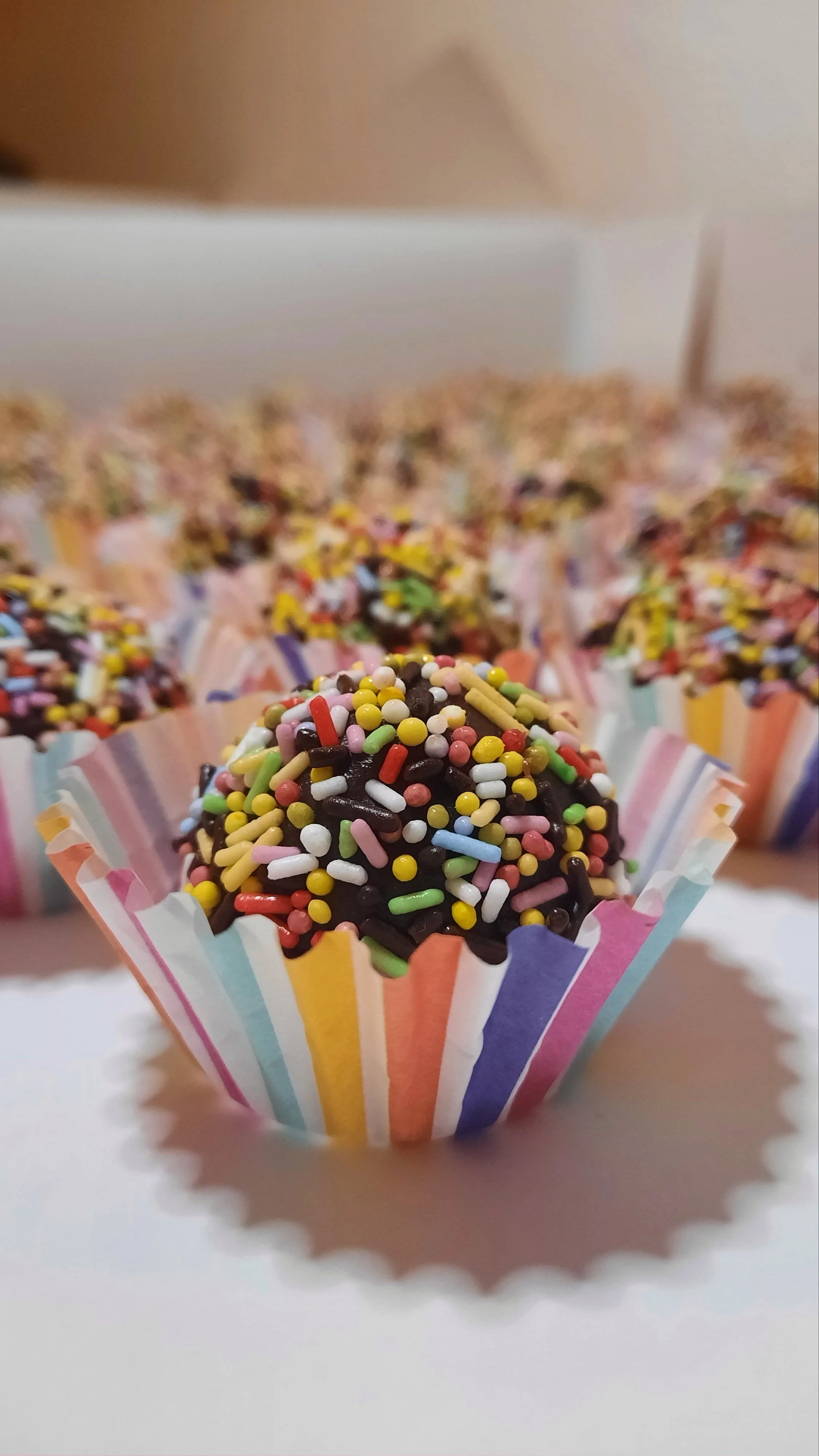 Une bouchée de gâteau au chocolat recouverte de sprinkles colorés dans une caissette en papier rayée pastel.