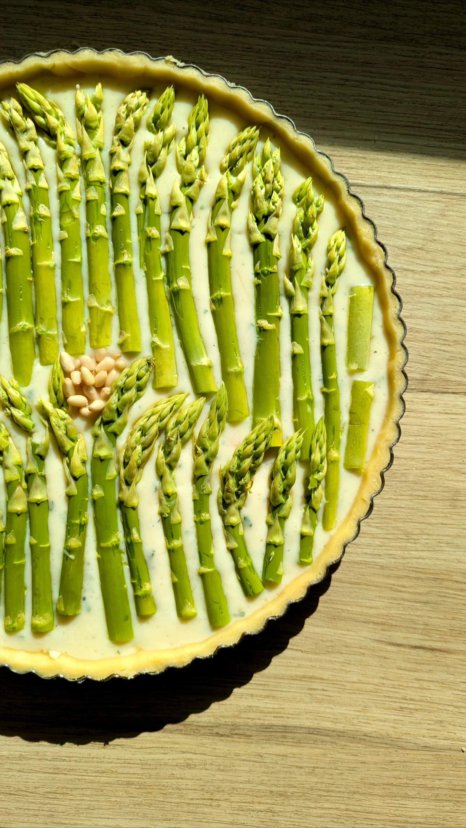 Tarte aux asperges avec une crème, décorée de quelques pignons de pin sur une surface en bois.