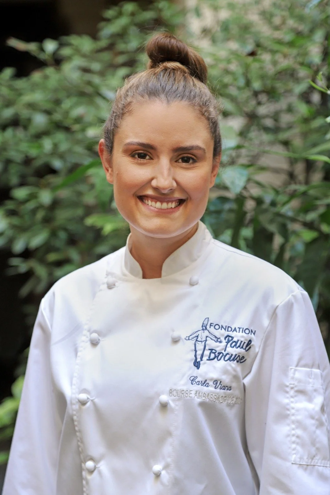 Carla Viana portant une veste de chef blanche avec une broderie indiquant la Fondation Paul Bocuse.
