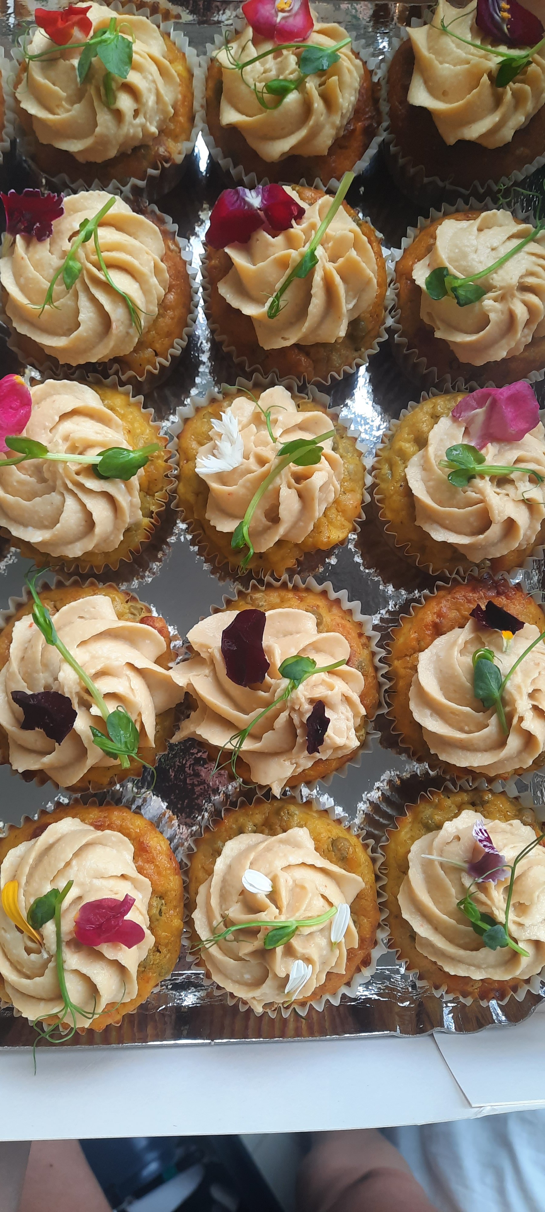 Mini cupcakes décorés avec une crème beige, garnis de petites fleurs et de feuilles vertes.