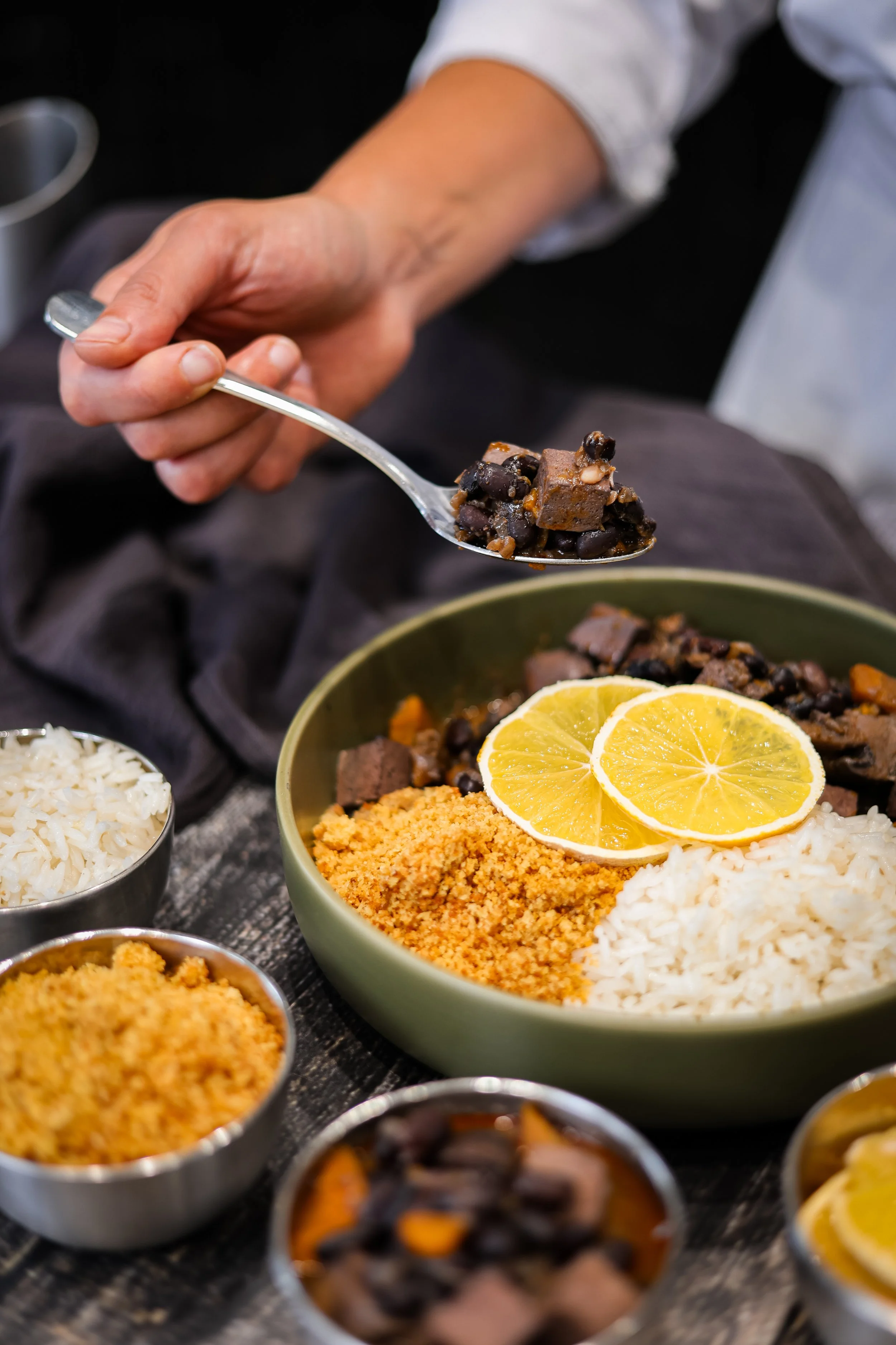 Un bol avec du riz blanc, un autre bol avec des tranches de citron, et plusieurs petits ramequins contenant diverses garnitures comme du crumble, des haricots noirs, et d'autres ingrédients pour un repas.