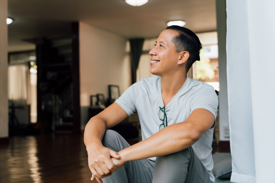 Man sitting by a window smiling and looking outside in a bright room.