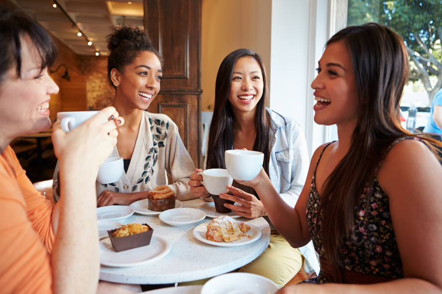 Four women enjoying coffee and pastries at a café table, smiling and talking.