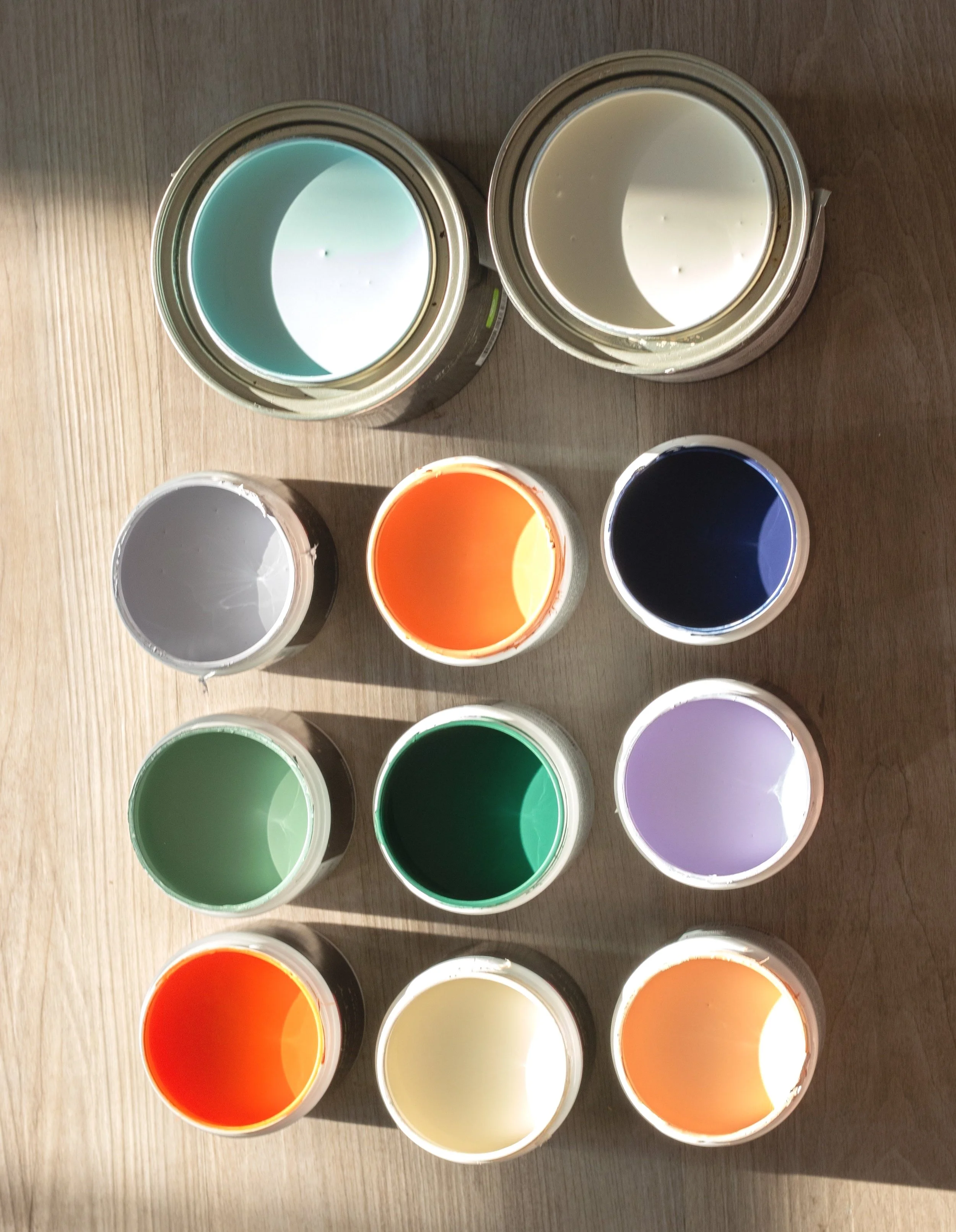 Nine open paint cans with various colors arranged on a wooden surface.