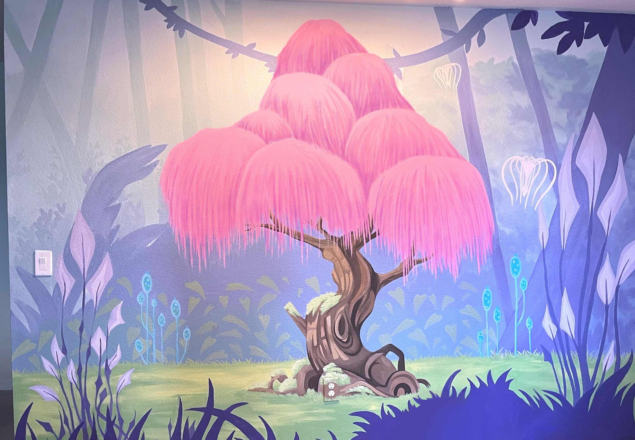 Colorful mural of a fantasy tree with a twisted trunk and large pink, hanging, umbrella-like foliage in a whimsical forest scene with blue and purple plants and glowing white flowers.