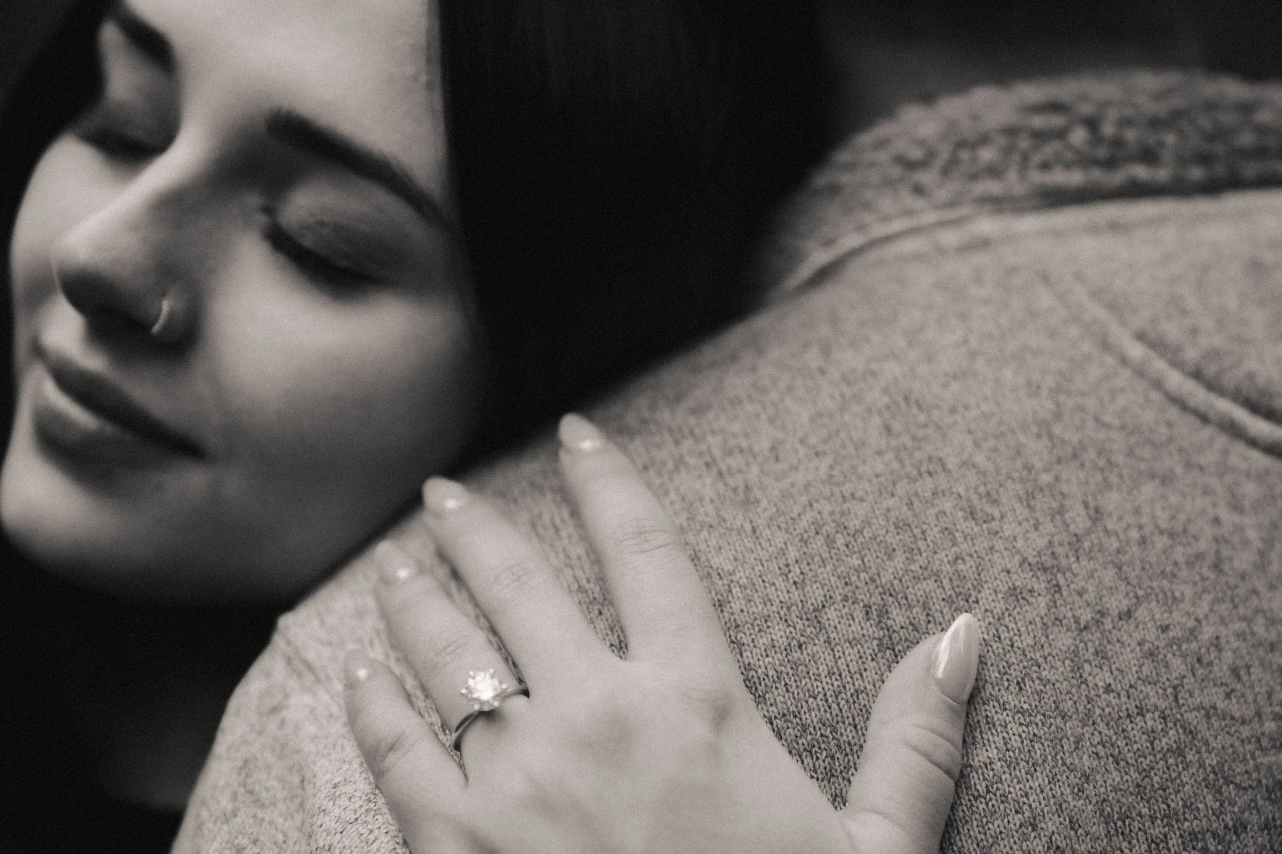 Close-up of a woman with closed eyes and a nose ring, resting her hand on someone's shoulder.