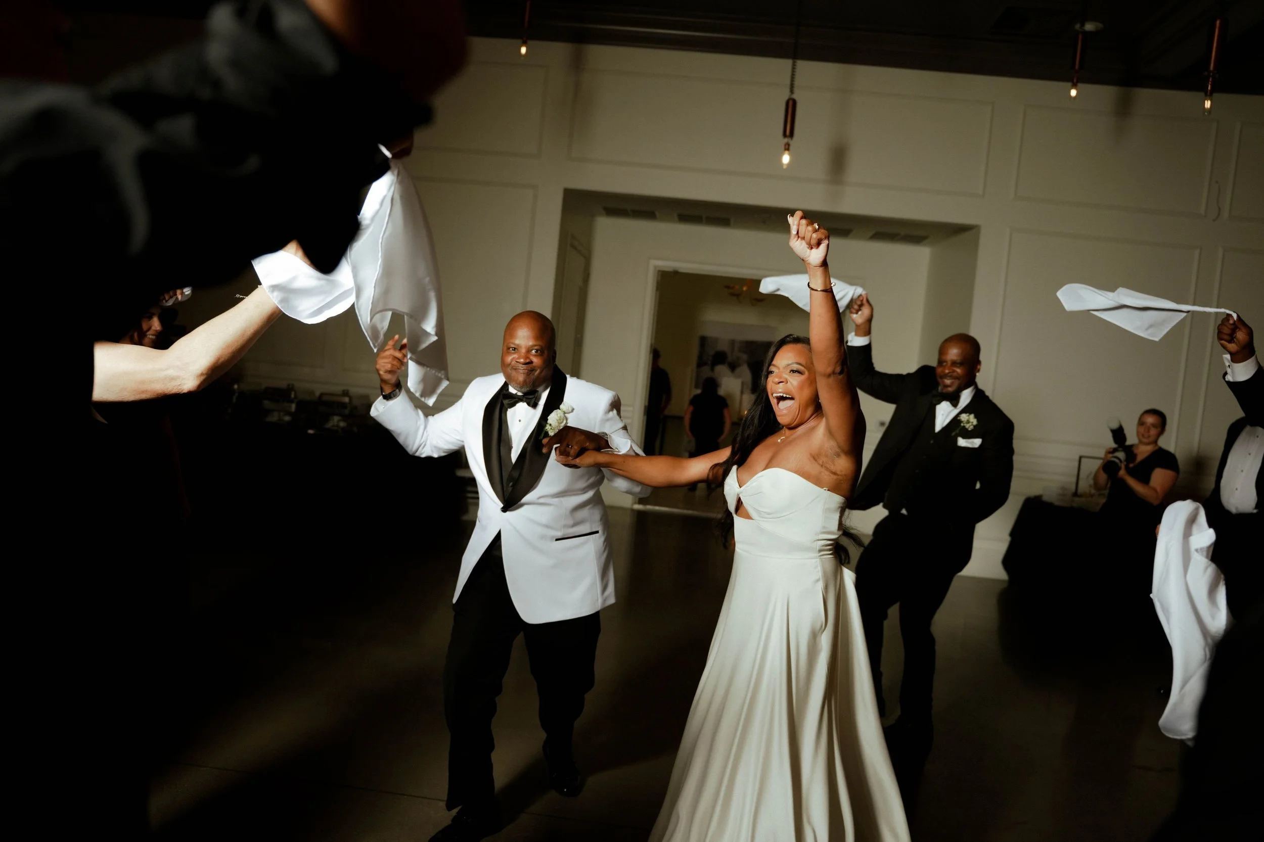 Joyful bride dancing with groom at wedding reception, surrounded by guests waving cloths