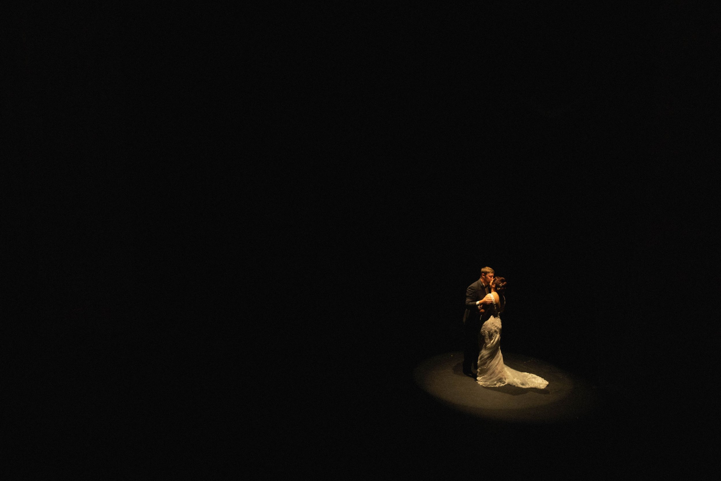A bride and groom dancing on a dark stage with a spotlight focused on them.
