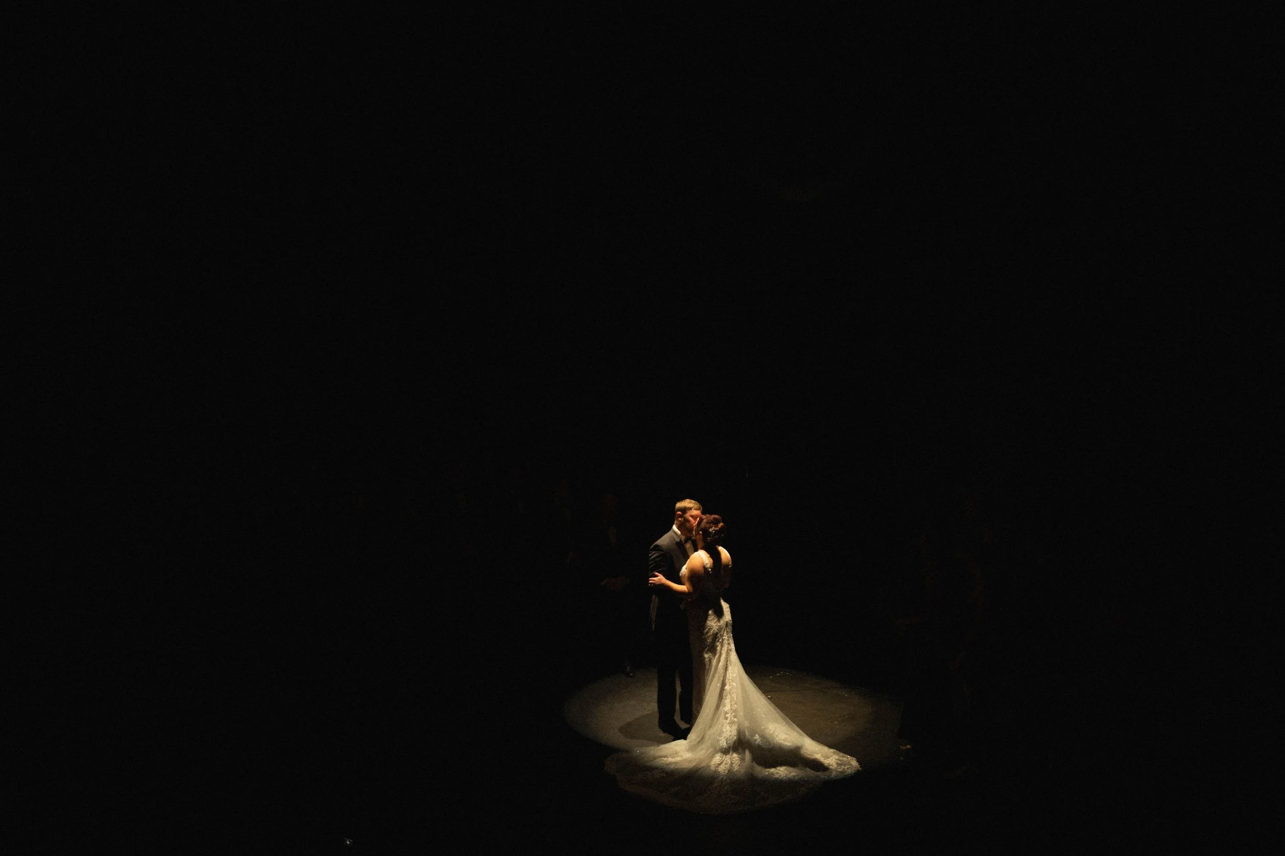 A bride and groom dancing in a spotlight at their wedding, surrounded by darkness.