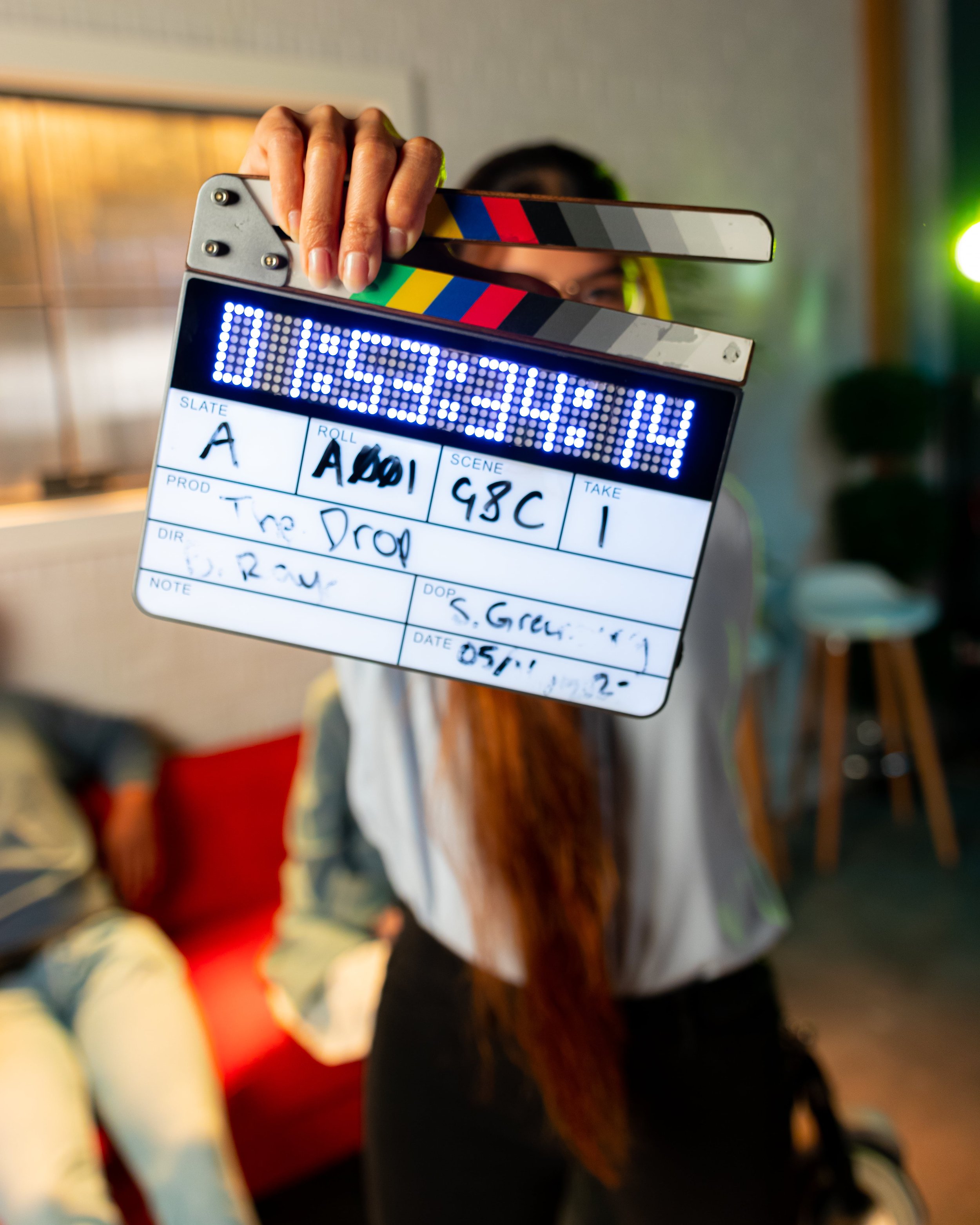 Close-up view of a person holding a clapperboard on a film set, with blurred background