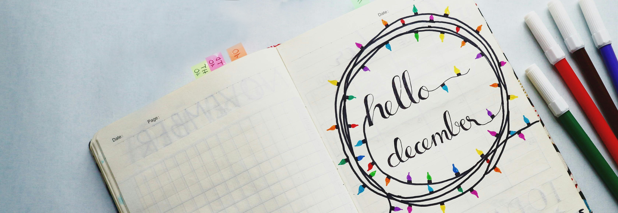 "Hello December" written in a journal with a marker. Words are enclosed in a doodle resembling a string of Christmas lights.