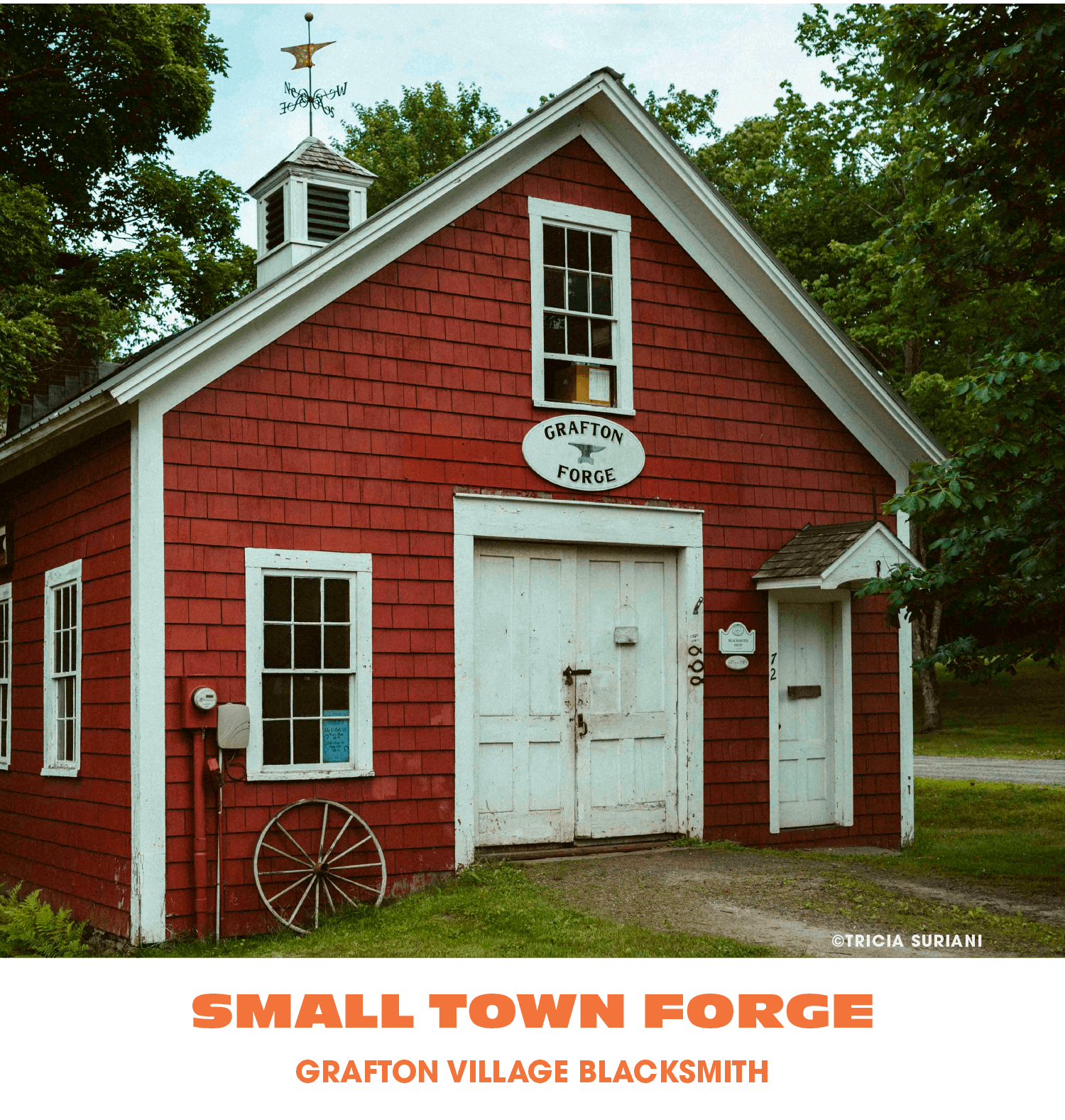 A small red wooden building with white trim, labeled as Grafton Village Blacksmith, featuring a large double door, several windows, a weather vane on the roof, and a vintage wagon wheel leaning against the wall. Surroundings include green trees and g