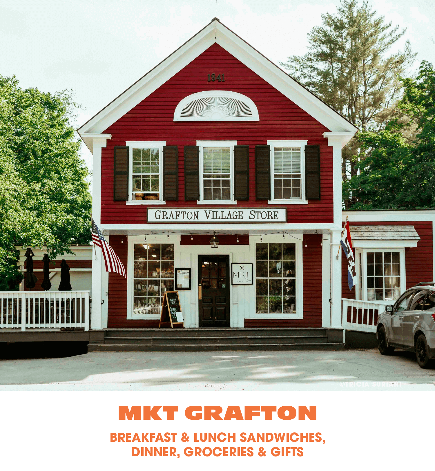 Red two-story building with white trim labeled Grafton Village Store, with American and state flags outside, and a sign for MKT Grafton in front.