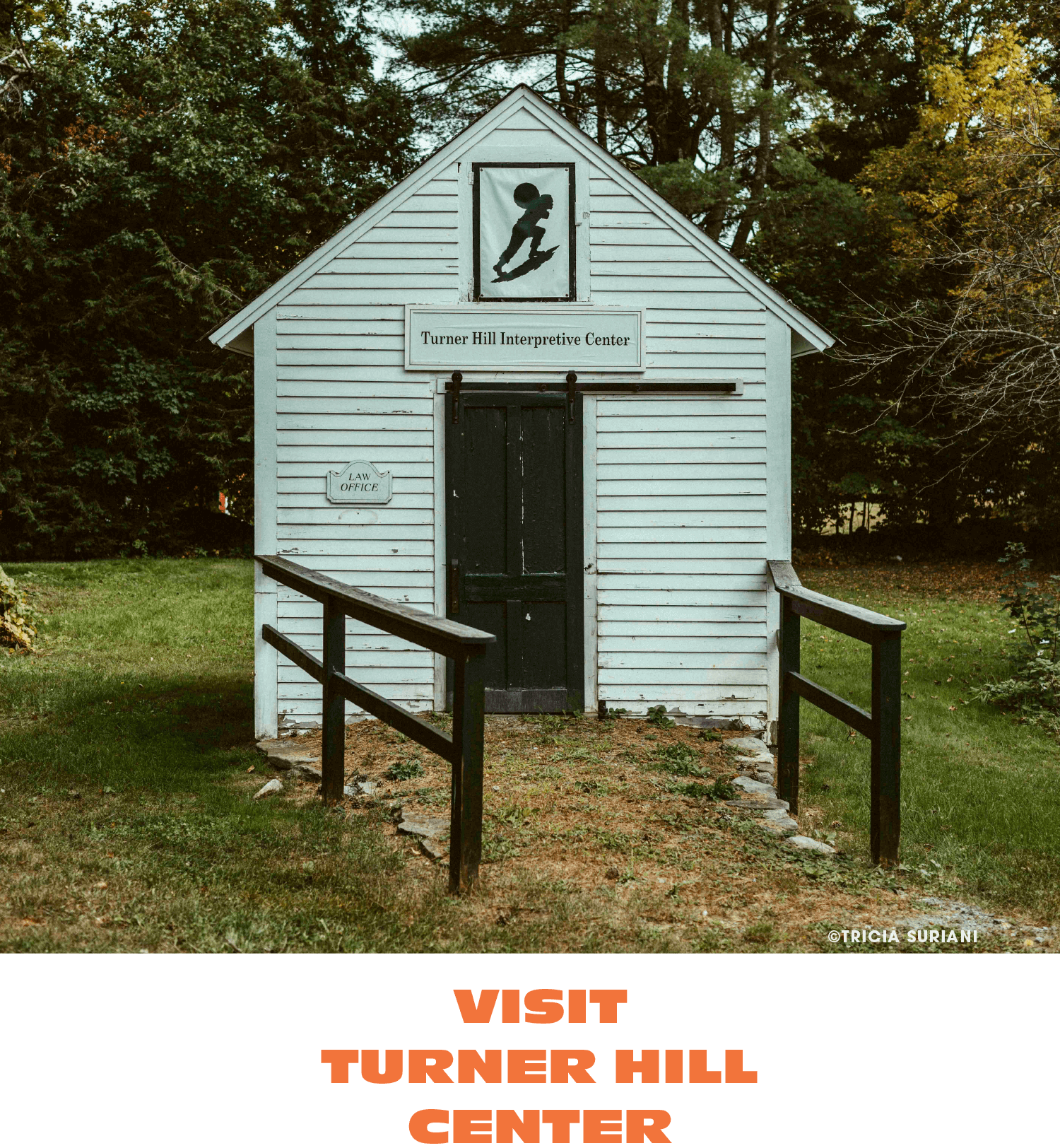 Small white wooden building with black door, black railings, and sign that reads 'Turner Hill Interpretive Center,' surrounded by trees.
