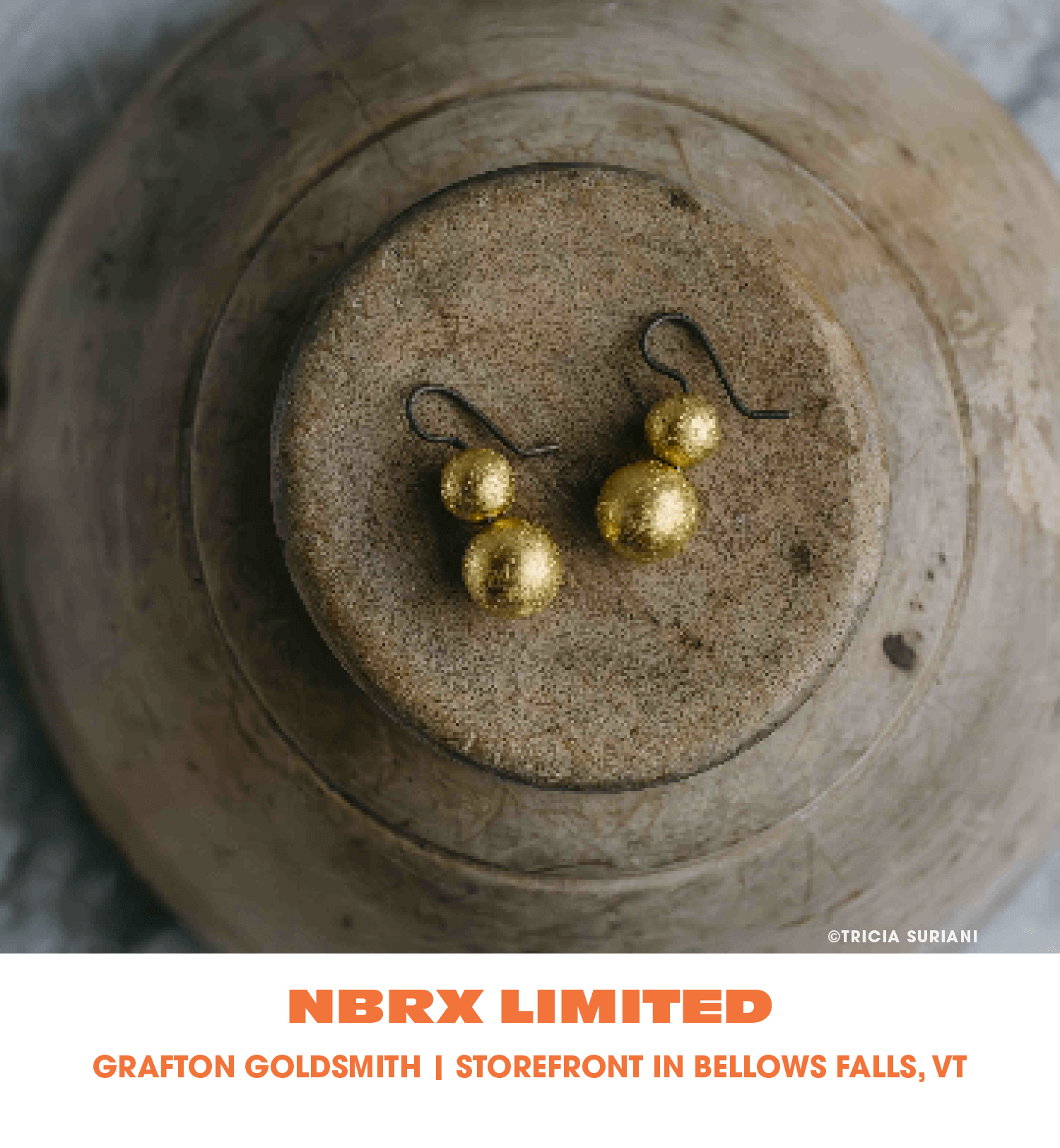 Gold dangling earrings with three spherical pendants, placed on a metallic surface