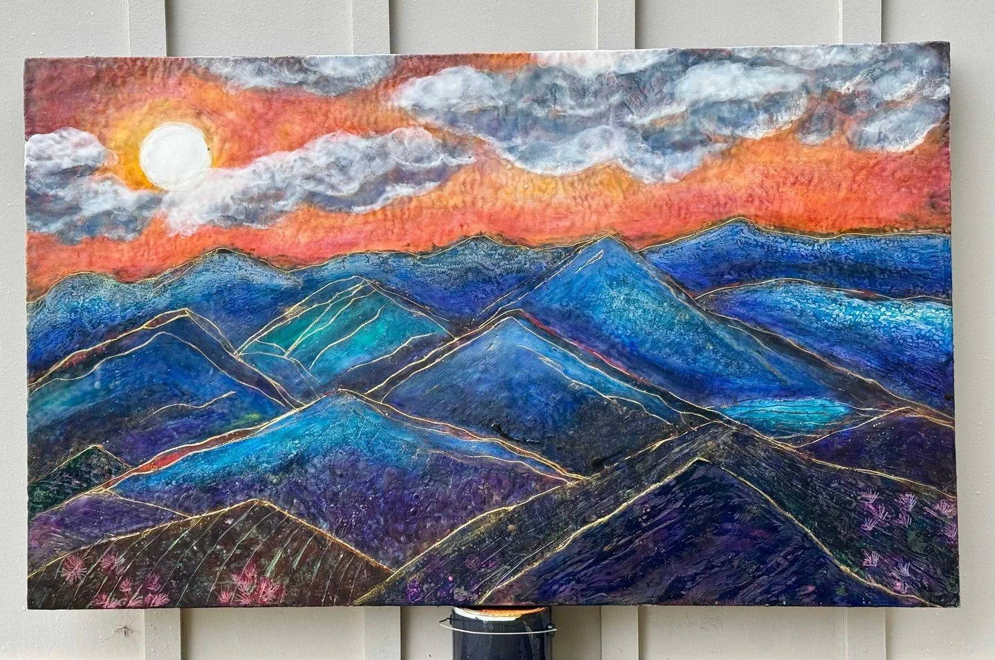Bring the beauty of a glowing sunset and majestic mountain peaks into your space with Sunset Blue Mountains by Emily Anne Scott.

Featuring rich blues, vibrant sunset hues, and delicate golden details, this original encaustic painting adds depth, war