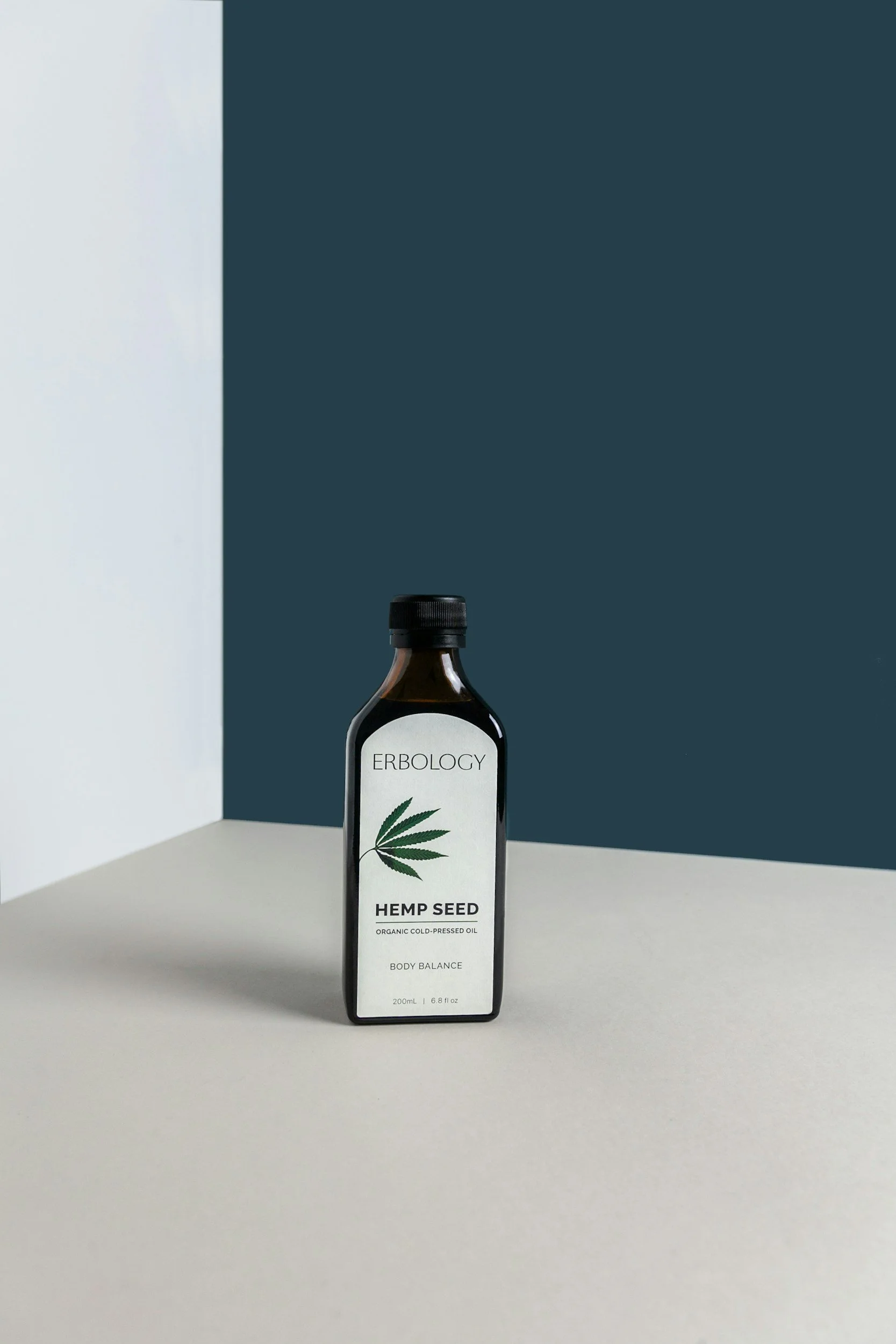 Dark glass bottle of Erbology hemp seed oil labeled "Organic Cold-Pressed Oil, Body Balance" on a minimalist background.