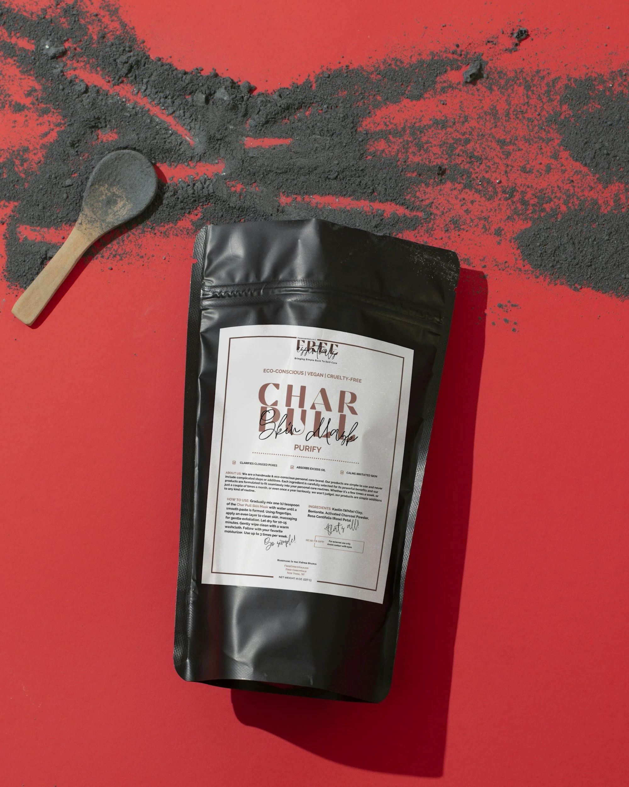 Charcoal powder on red surface with small wooden spoon and black packaging.