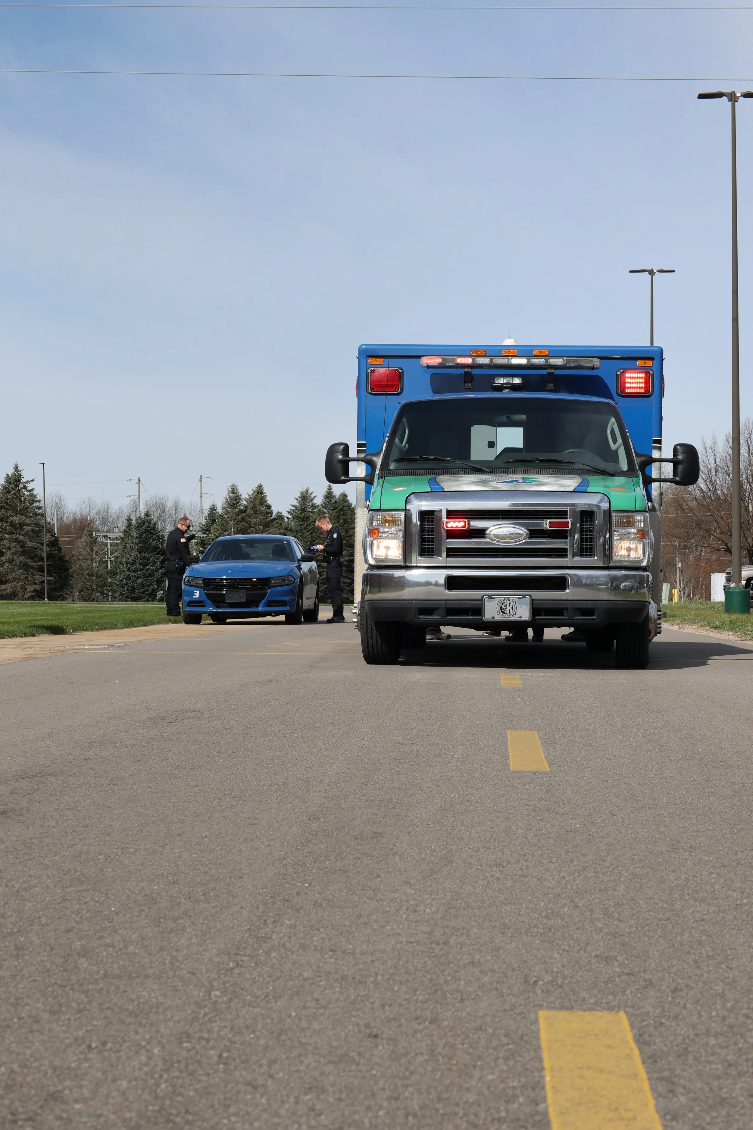 Ambulance and police car on the road with officers nearby.