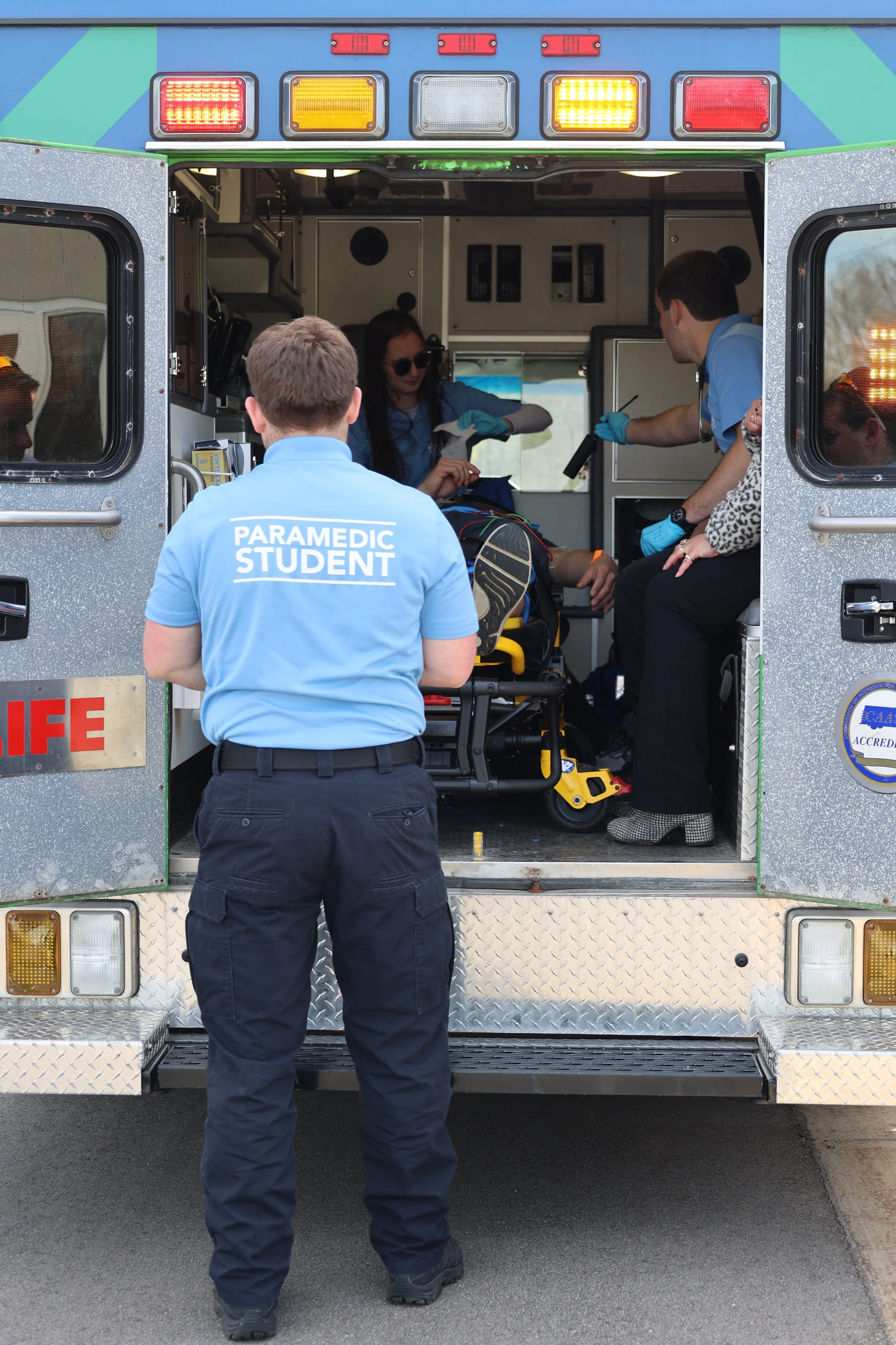 Paramedic students inside an ambulance attending to a patient on a stretcher.