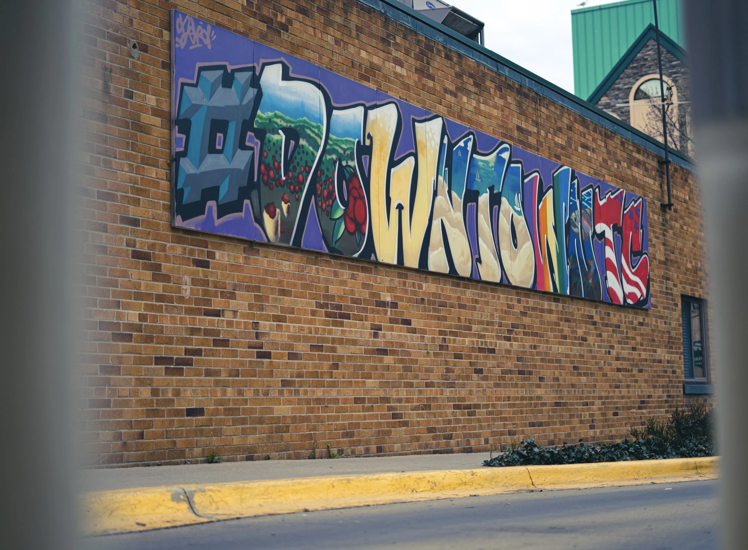 Colorful graffiti mural on a brick wall, featuring abstract shapes and patterns.